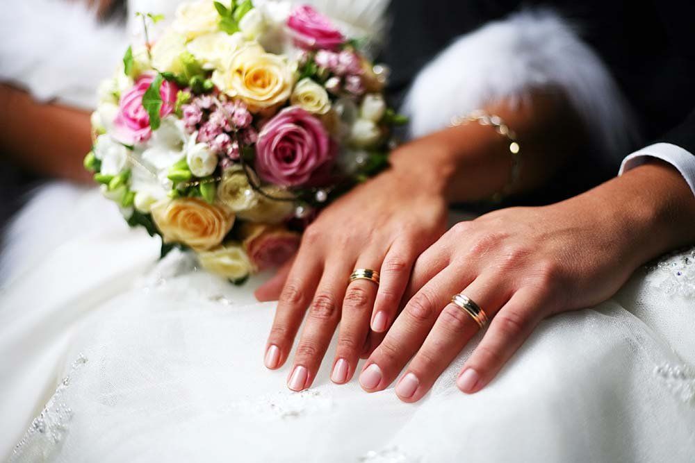 Wedding bouquet and hands with rings resting on a white dress