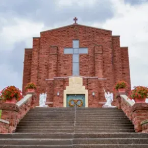 Brick church facade with a large cross above steps and flower planters on both sides