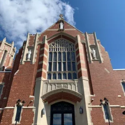 Gothic-style red brick building facade with tall arched windows against a blue sky