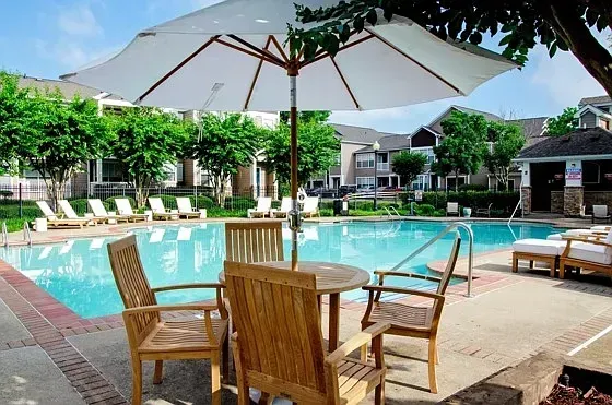 Resort-style swimming pool with lounge chairs and a table with chairs under an umbrella at Woodland Pointe in Nashville, TN.