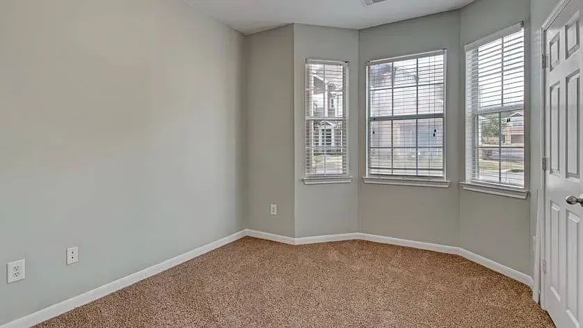 Empty room with neutral-colored walls, carpet, and blinds on windows at Woodland Pointe in Nashville, TN.