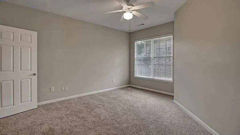 Bedroom with plush carpet, ceiling fan, and large window with blinds at Woodland Pointe in Nashville, TN.