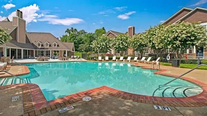 Large outdoor swimming pool with lounge chairs, brick deck, and clubhouse under a blue sky at Woodland Pointe Residences.