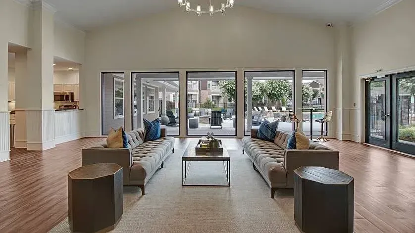 Luxurious apartment community clubhouse lounge area with plush seating, modern coffee table, and large windows overlooking the pool and outdoor amenities at Woodland Pointe in Nashville, TN.