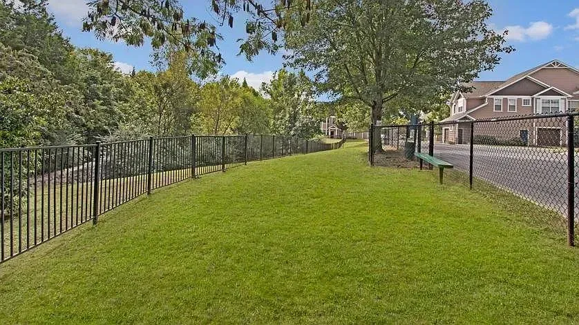 Fenced-in grassy area with a bench, surrounded by trees and apartment buildings at Woodland Pointe in Nashville, TN.