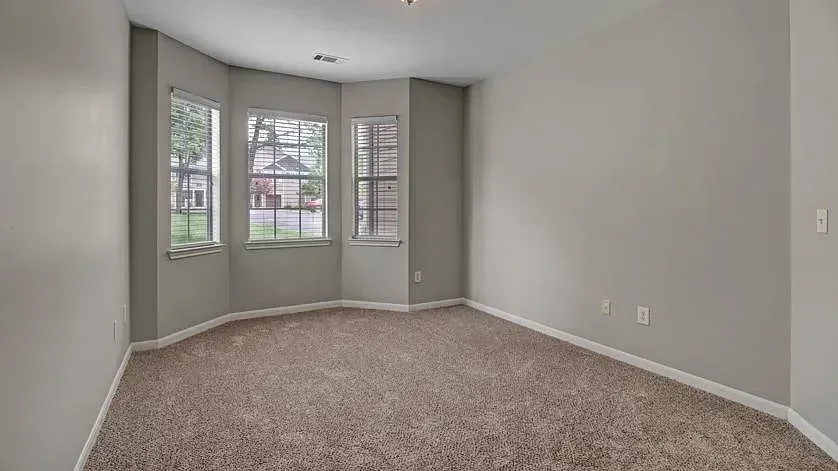 Empty bedroom with neutral gray walls and beige carpet, featuring a bay window with blinds at Woodland Pointe in Nashville, TN.