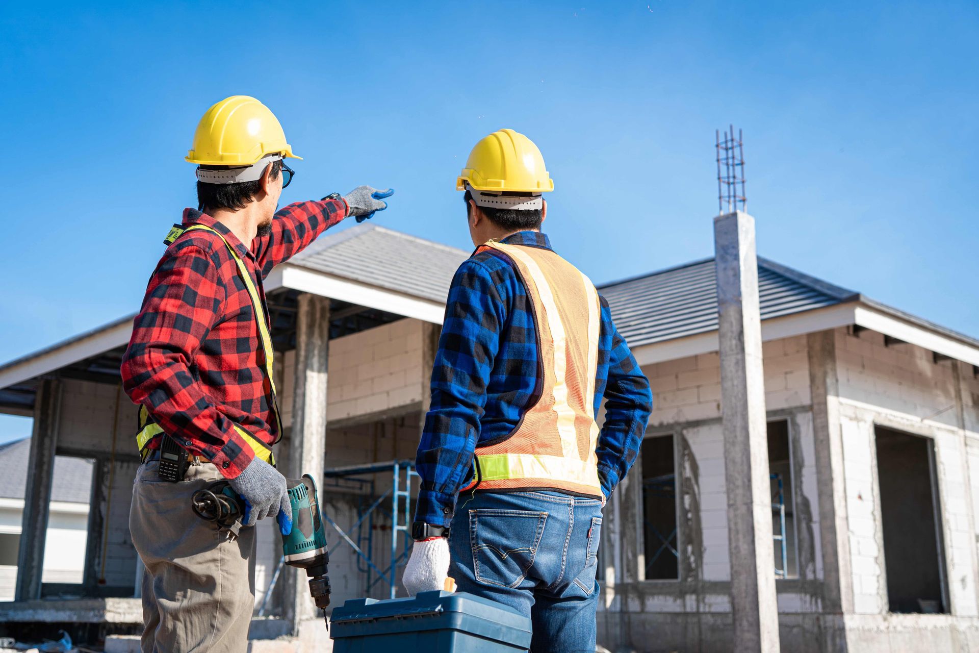 Two construction workers are standing in front of a house under construction