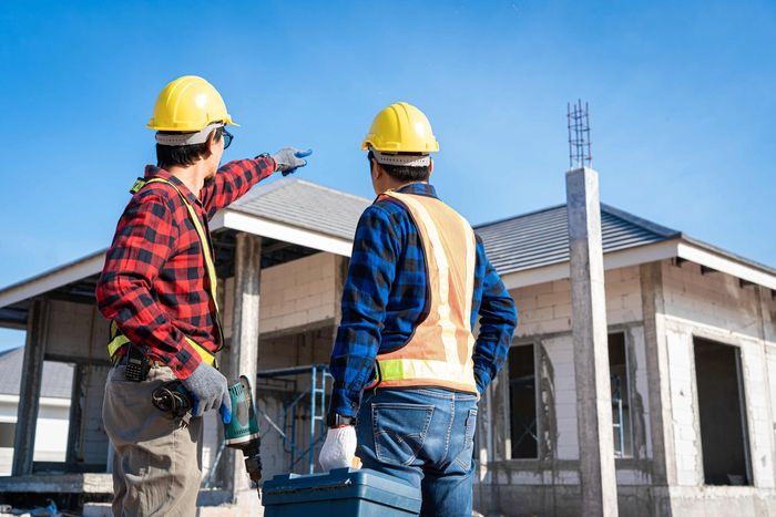 Two construction workers are standing in front of a house under construction