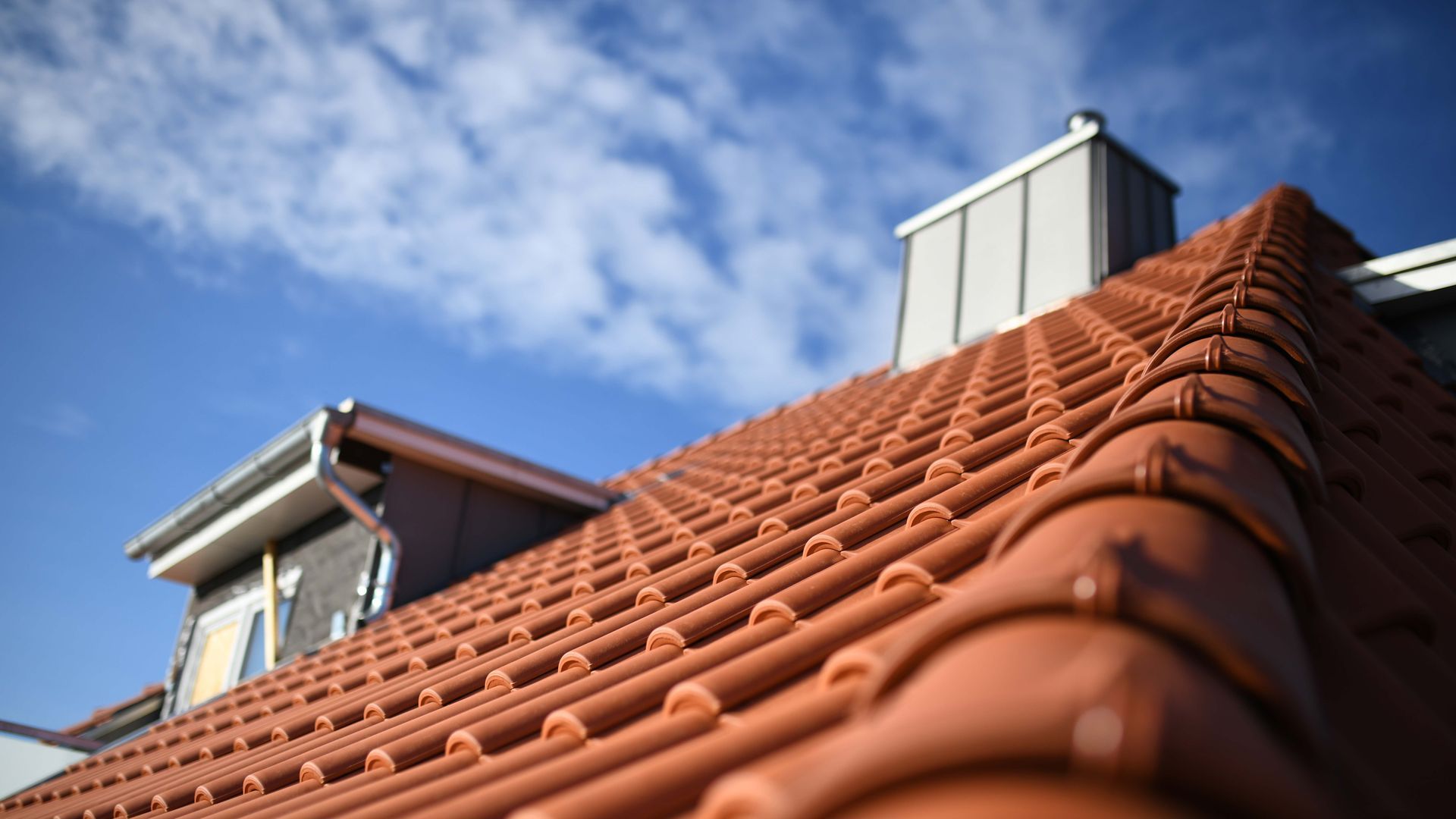 A close up of a red tiled roof with a chimney on top of it