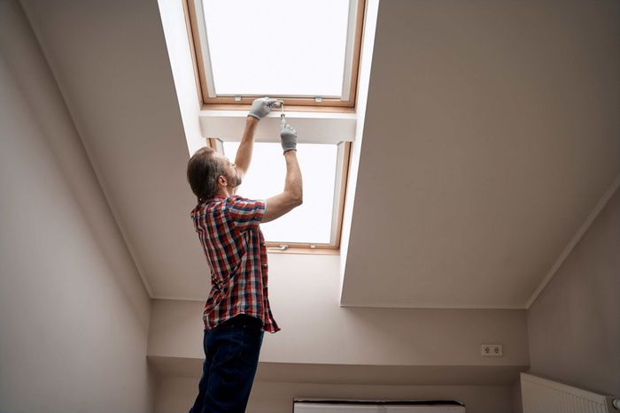 A man is installing a skylight in a room