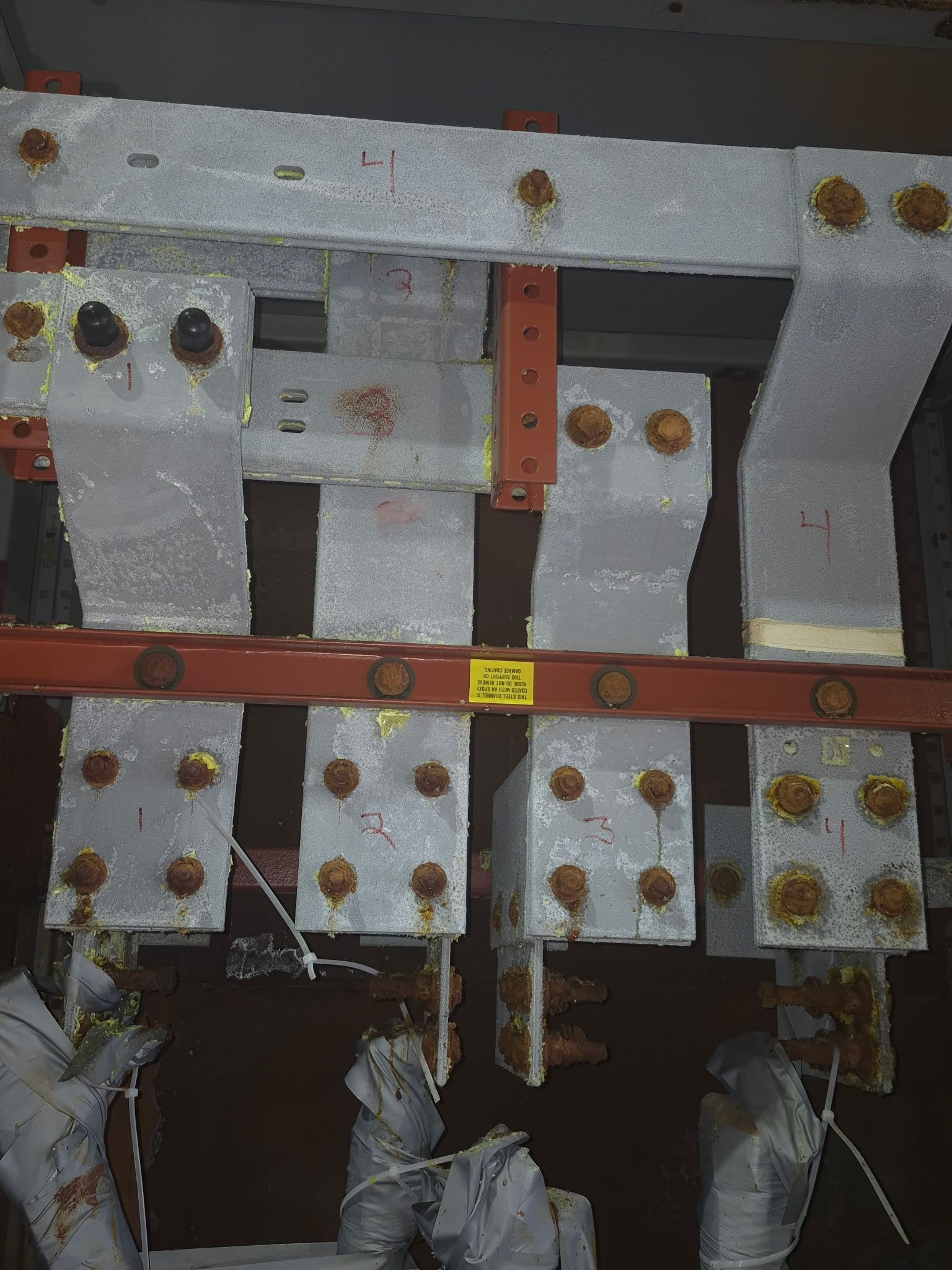 Close-up of electrical busbar systems featuring multiple thick metal conductors mounted with bolts on a red frame.