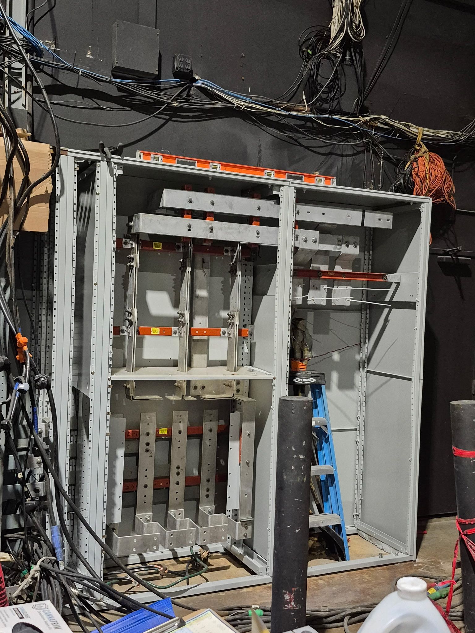 An open industrial electrical switchgear cabinet showing internal copper busbars and wiring in a room with exposed cabling.