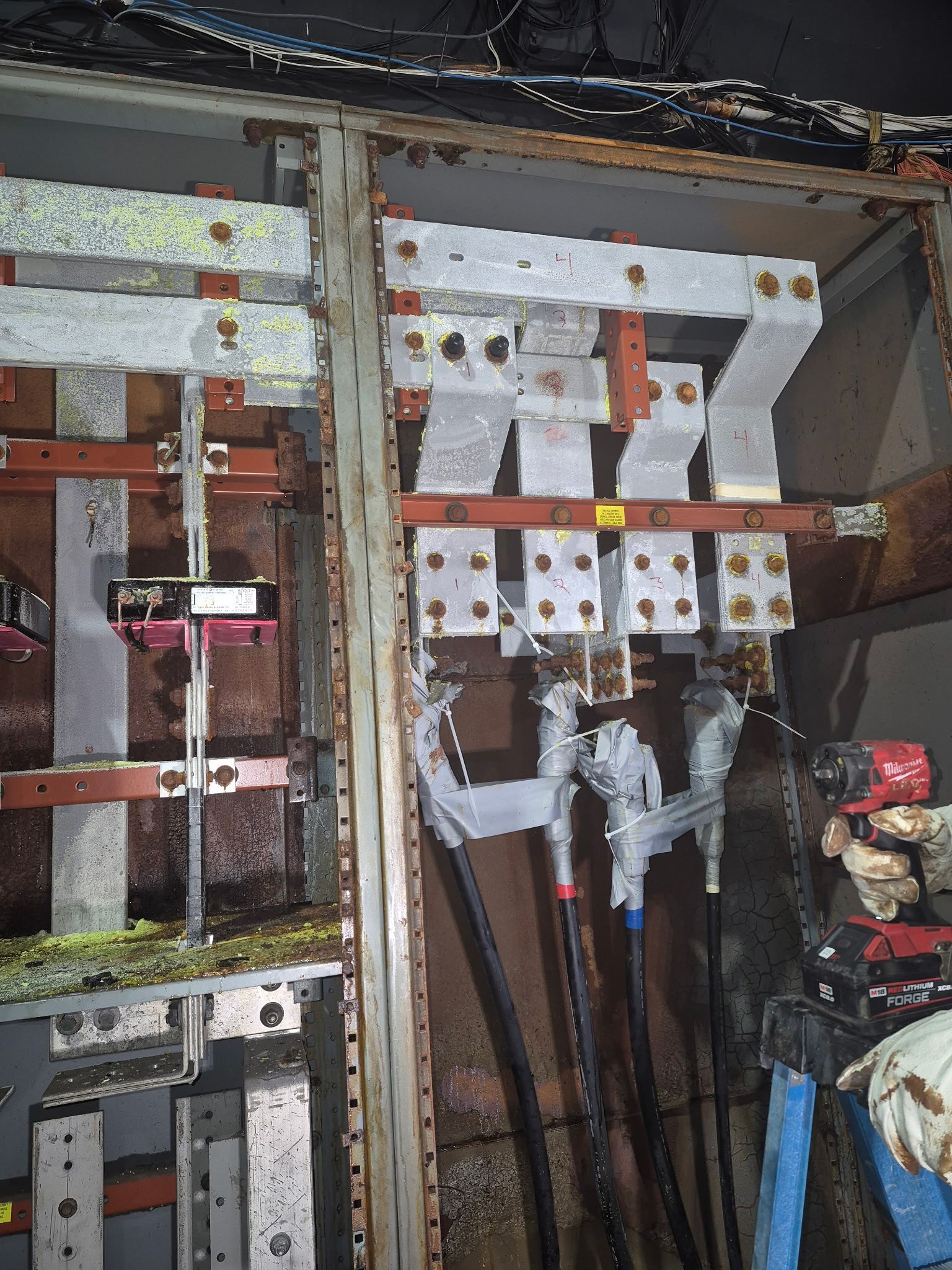 An electrical panel interior showing heavy metal busbars connected to thick black cables with metallic heat-shrink sleeves.