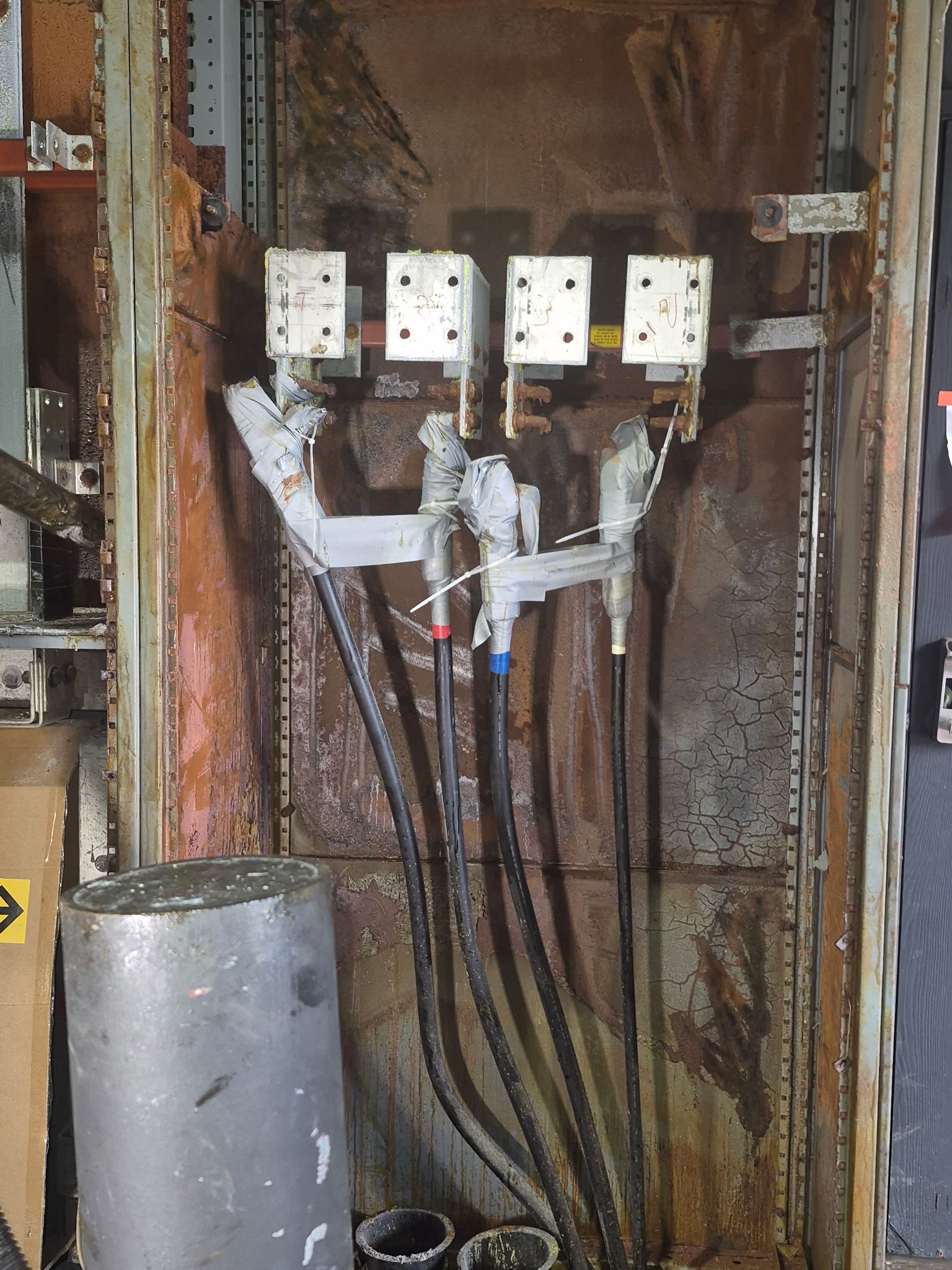 Internal view of a weathered electrical panel with four bus bar connectors wired to thick black cables.
