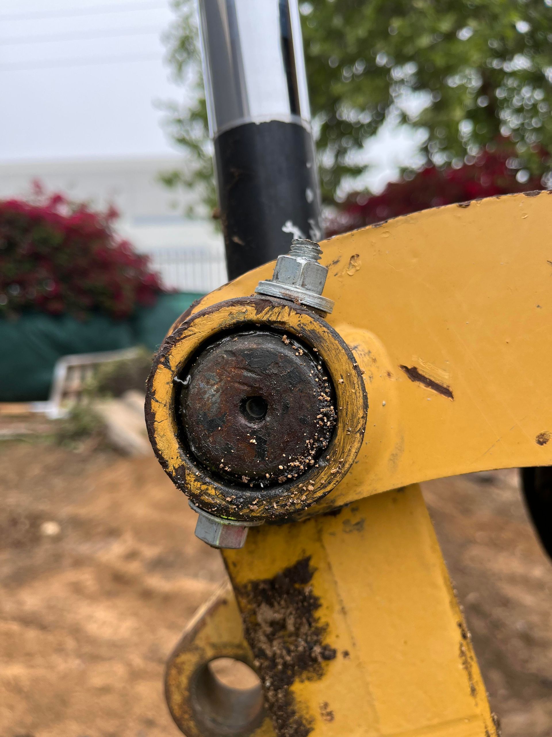 Close-up of a yellow construction equipment joint with a rusty pin and a damaged metal grease fitting.