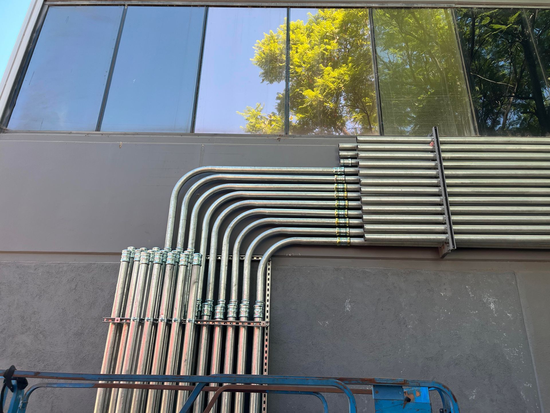 A series of parallel metal electrical conduits bent at ninety-degree angles along the exterior wall of a building.