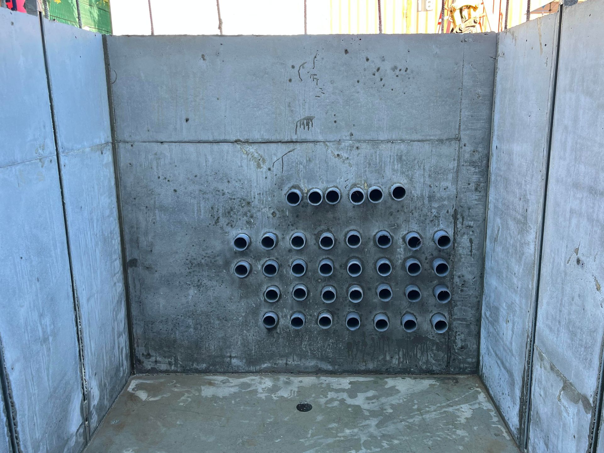 A gray concrete wall featuring a grid of small, protruding circular pipe openings in an unfinished construction site.