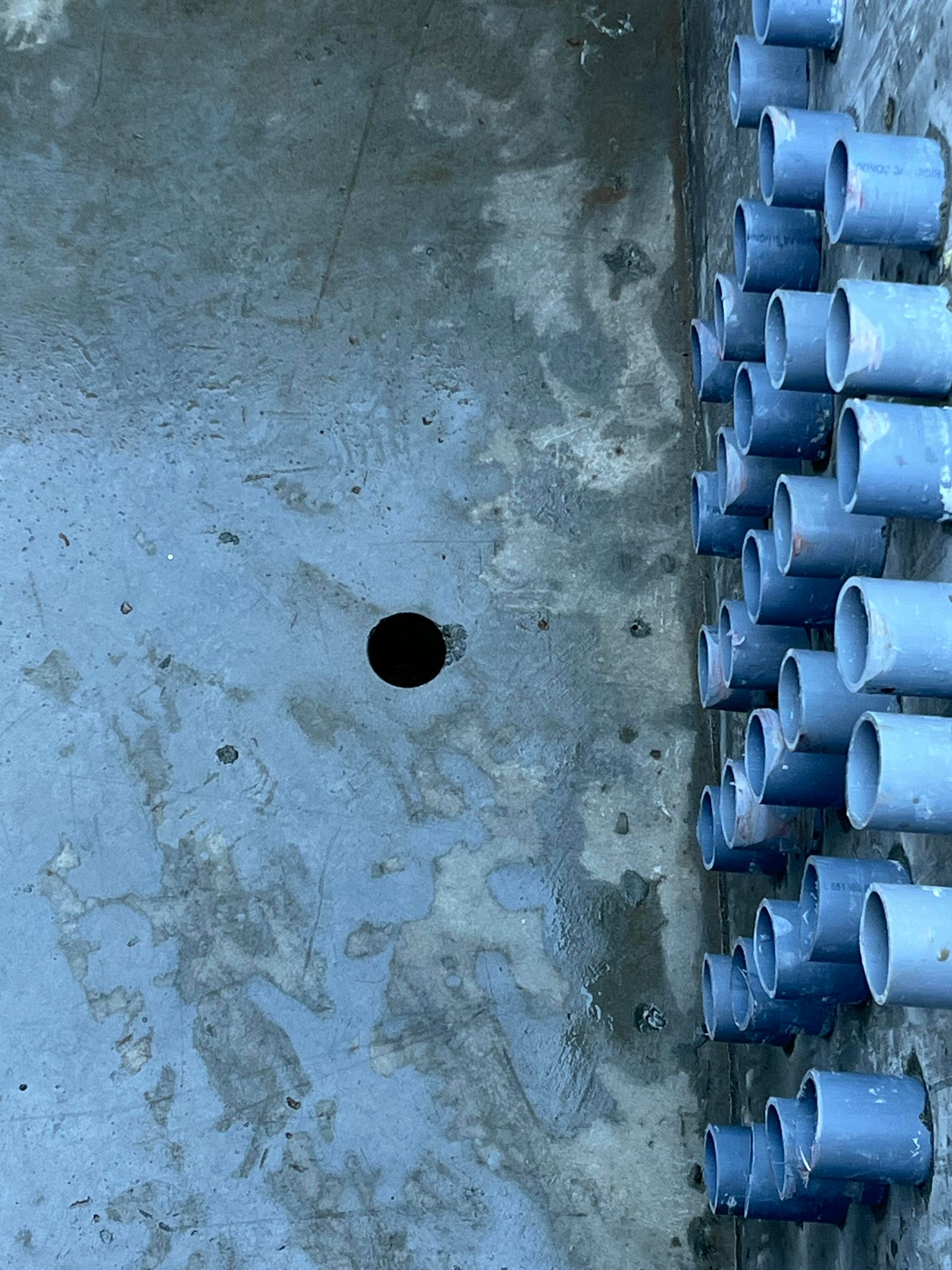 A vertical row of blue plastic pipes set into a gray concrete wall next to a single circular hole.
