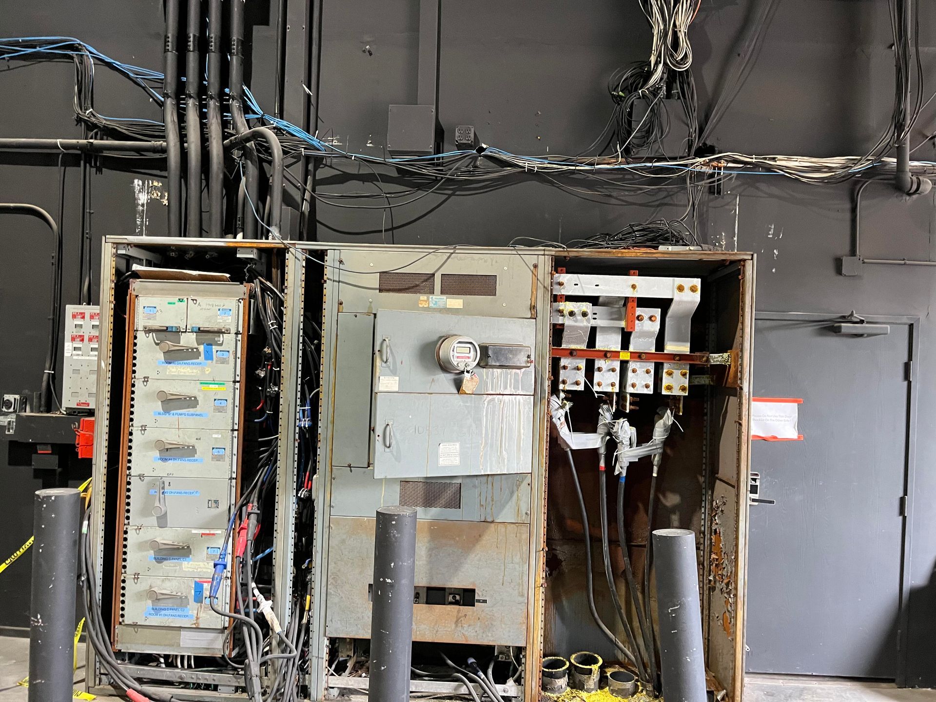 An industrial electrical panel with exposed wiring and open metal enclosures against a dark wall.
