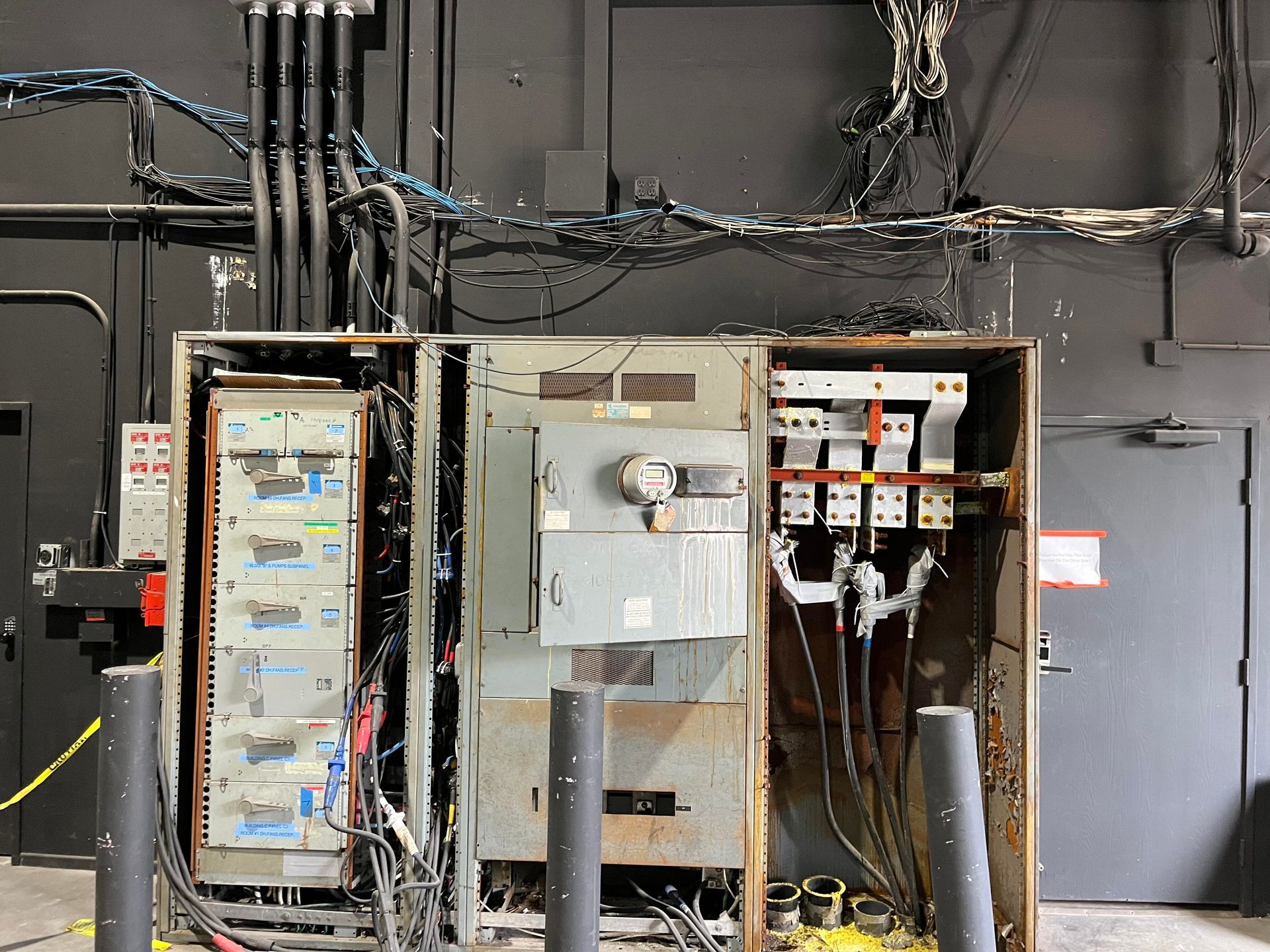 An open electrical switchgear cabinet featuring exposed wires, metal components, and heavy-duty conduits against a wall.