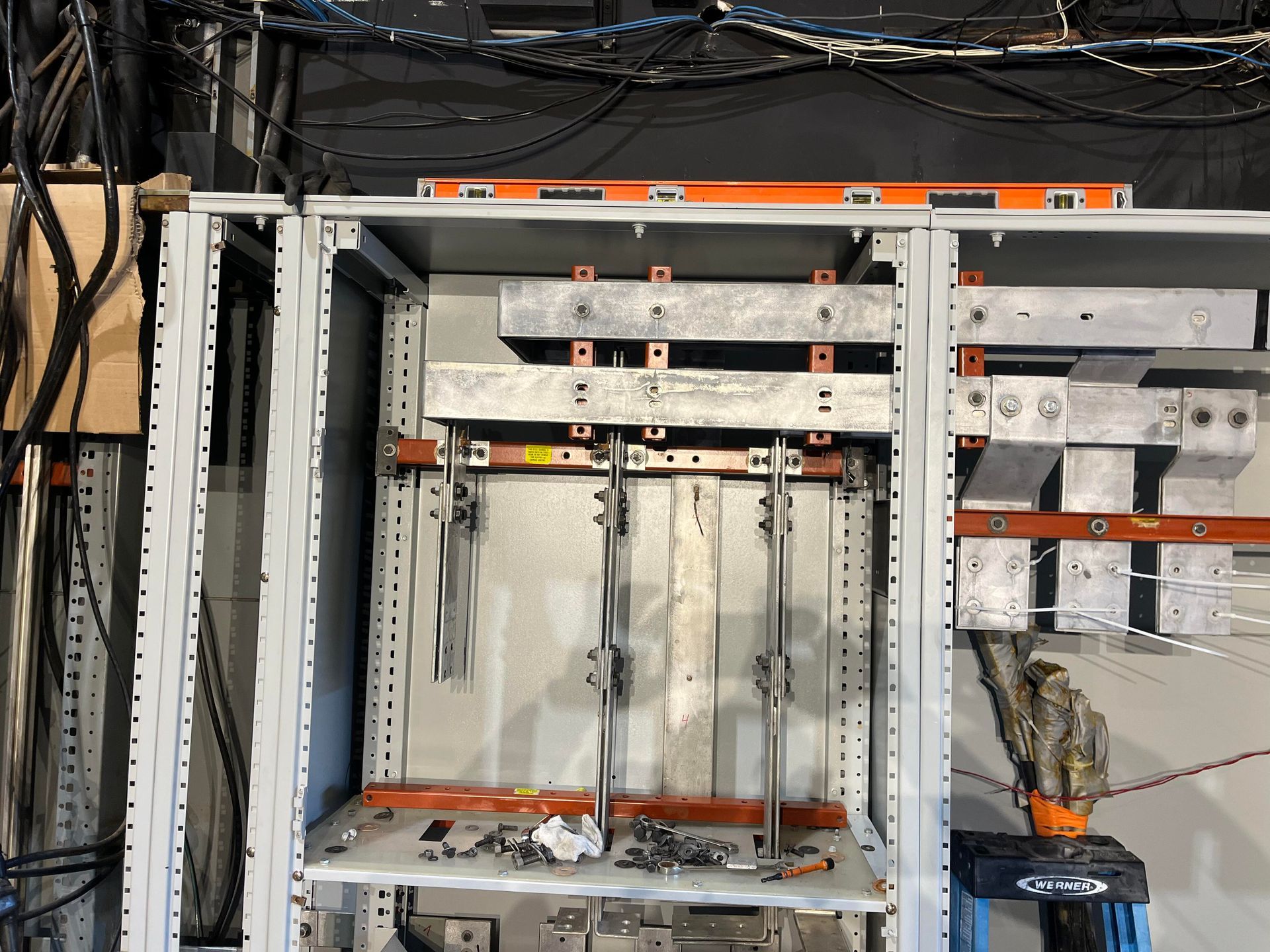 Open electrical panel enclosure with silver busbars, orange insulators, and wire bundles against a dark background.