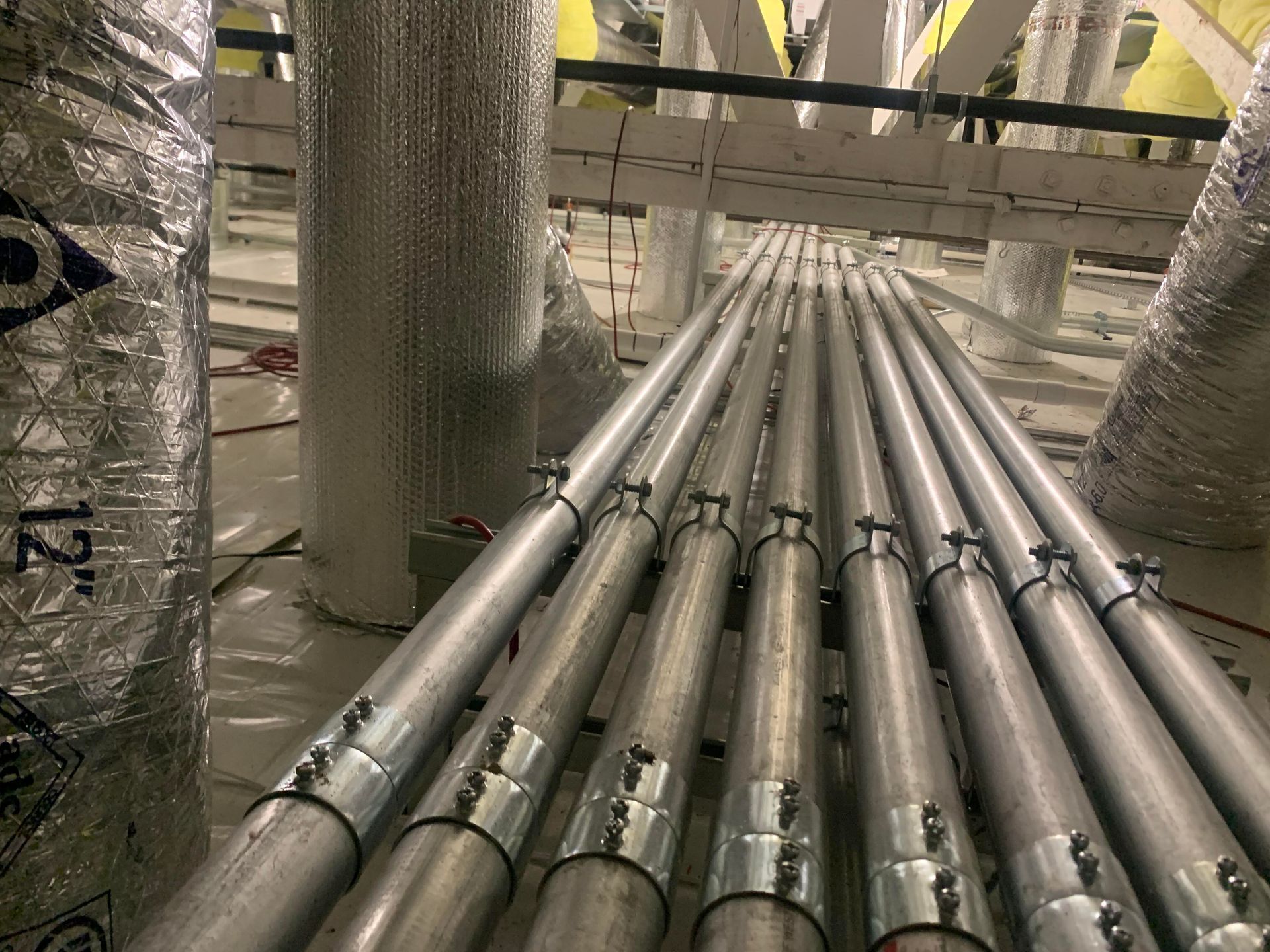 Several parallel metal electrical conduits with silver coupling joints run through an industrial ceiling space.