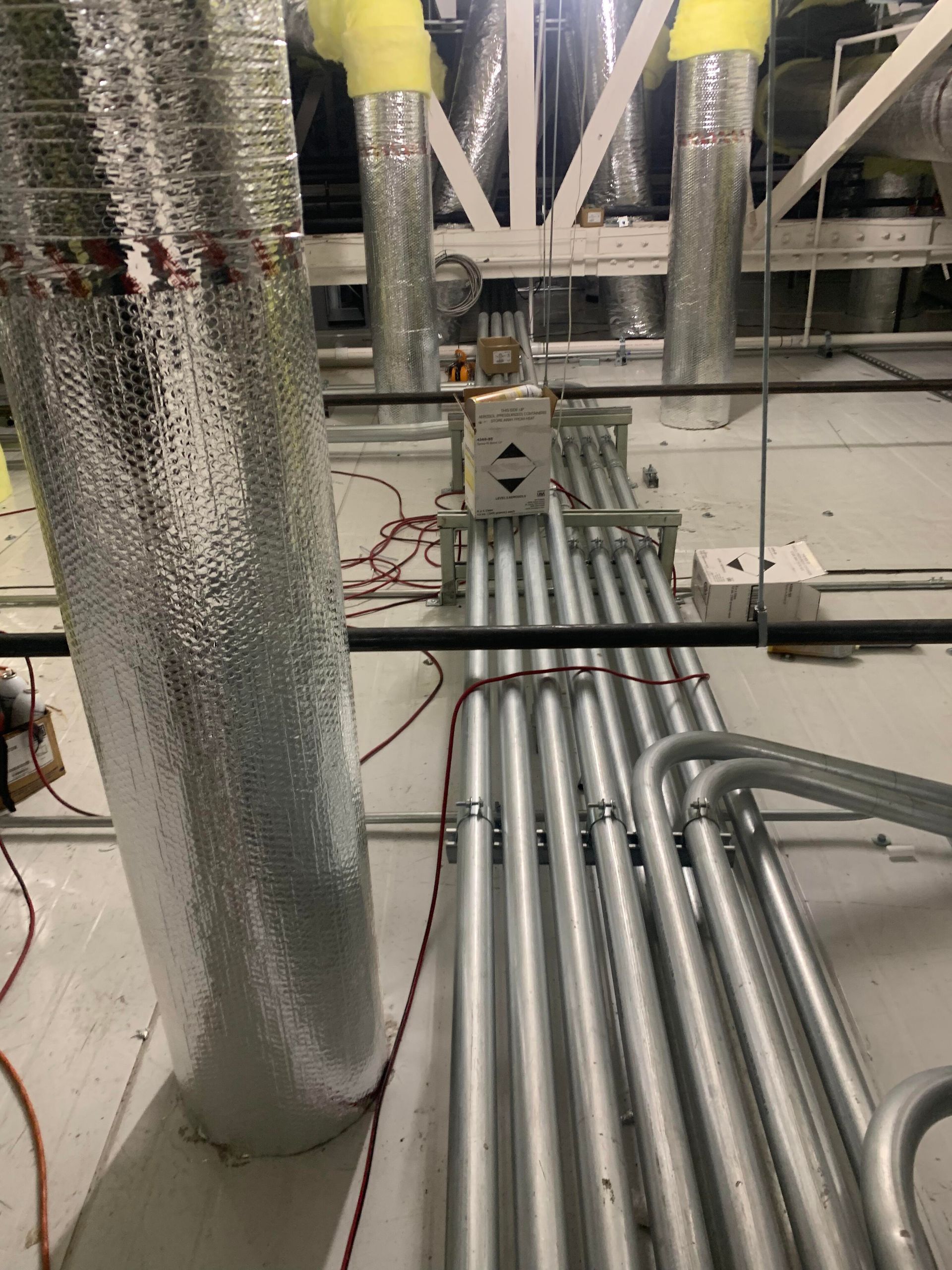 A view from above showing silver metal conduits and large insulated pipes running across an industrial ceiling.