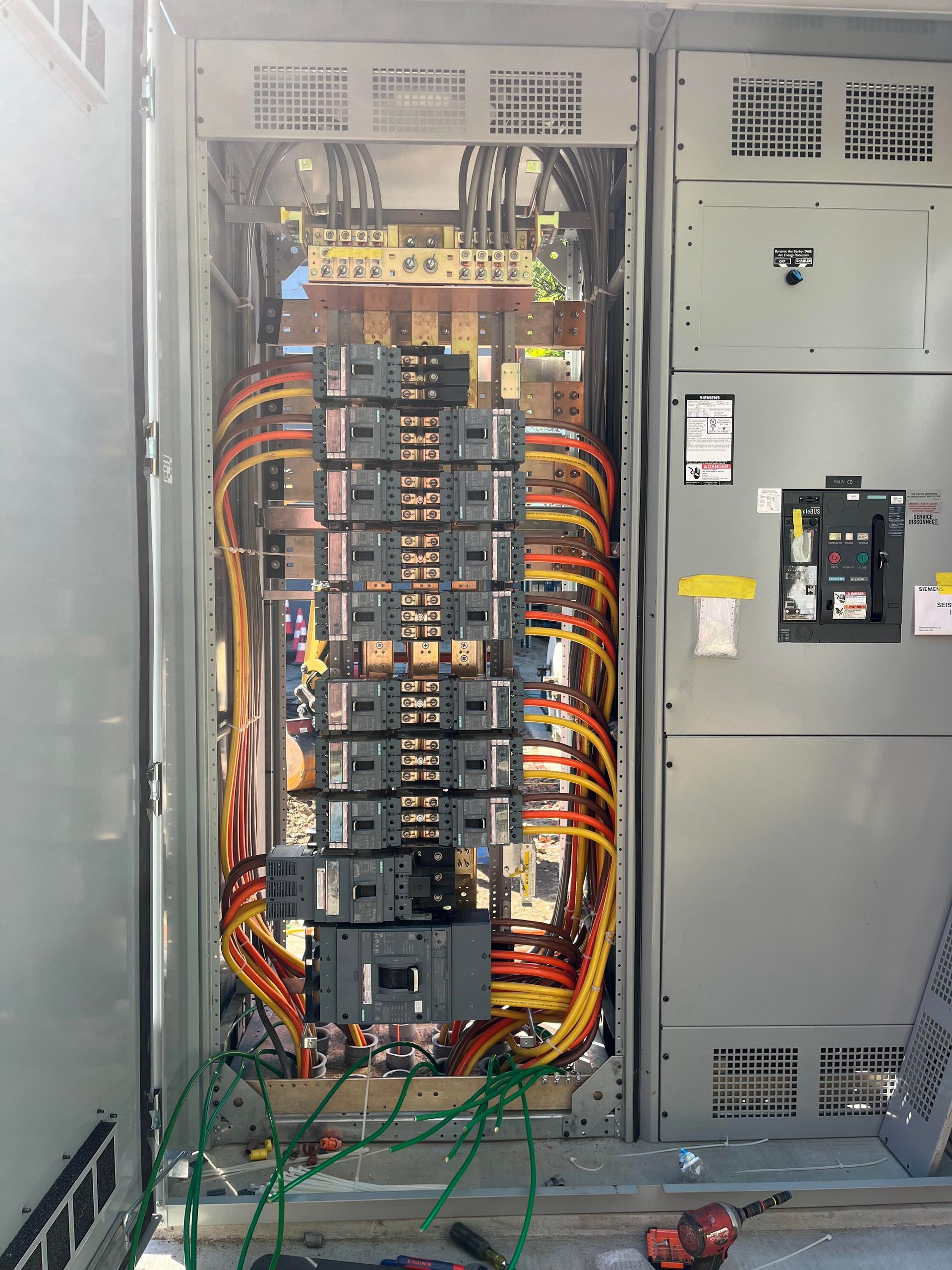 An open electrical distribution panel with multiple breakers and neatly bundled yellow and orange wiring inside a cabinet.