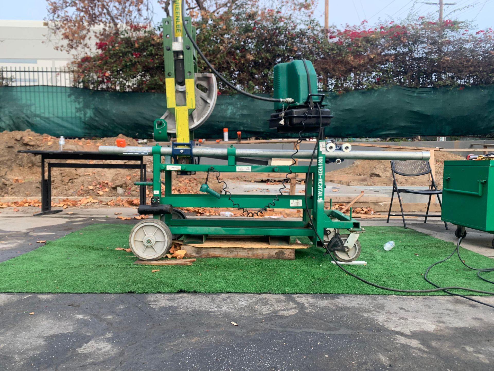 A green industrial pipe-cutting machine sits on an artificial turf mat in an outdoor construction area.