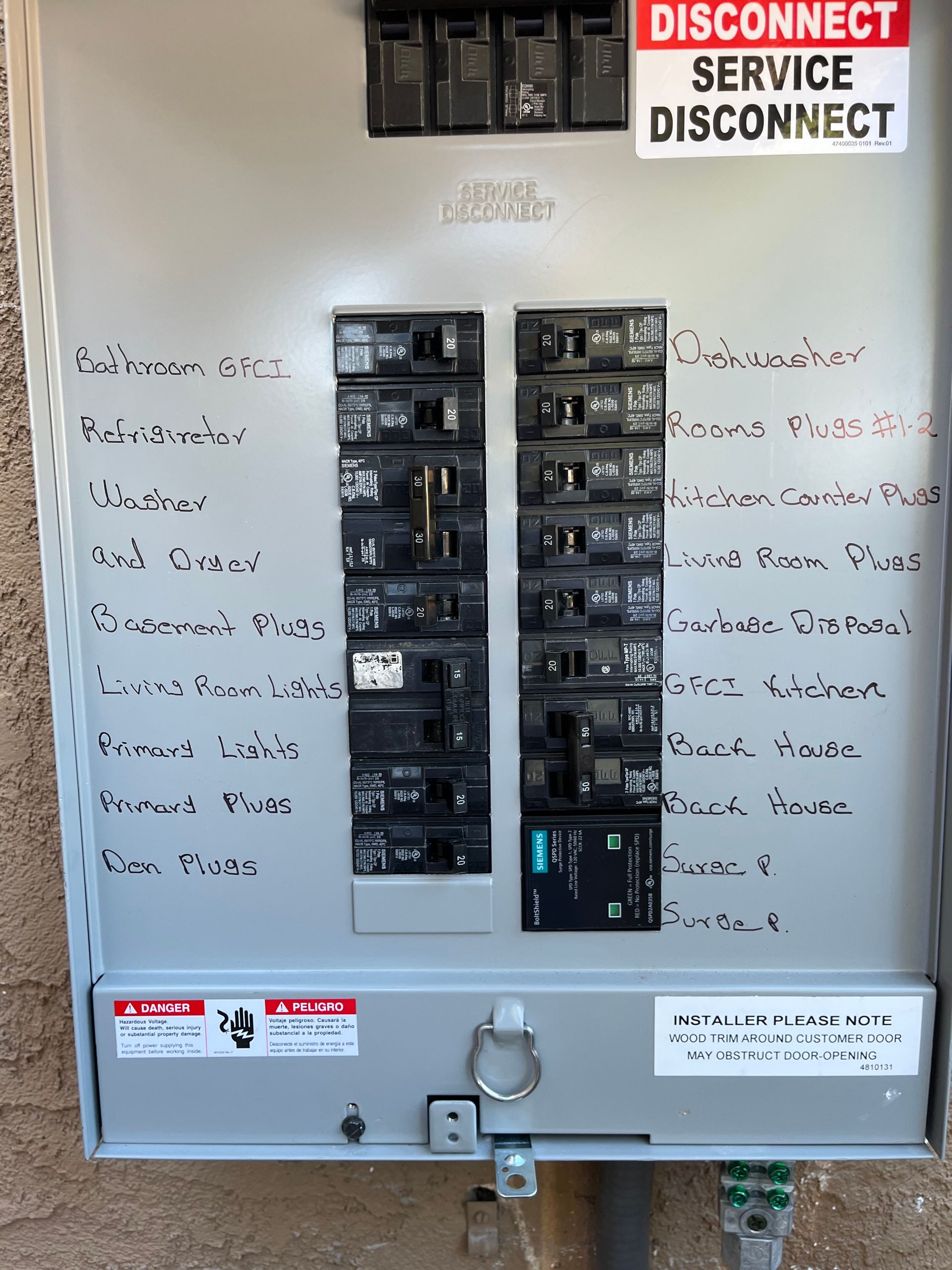 A gray residential electrical breaker panel with a service disconnect switch at the top and handwritten labels next to switches.