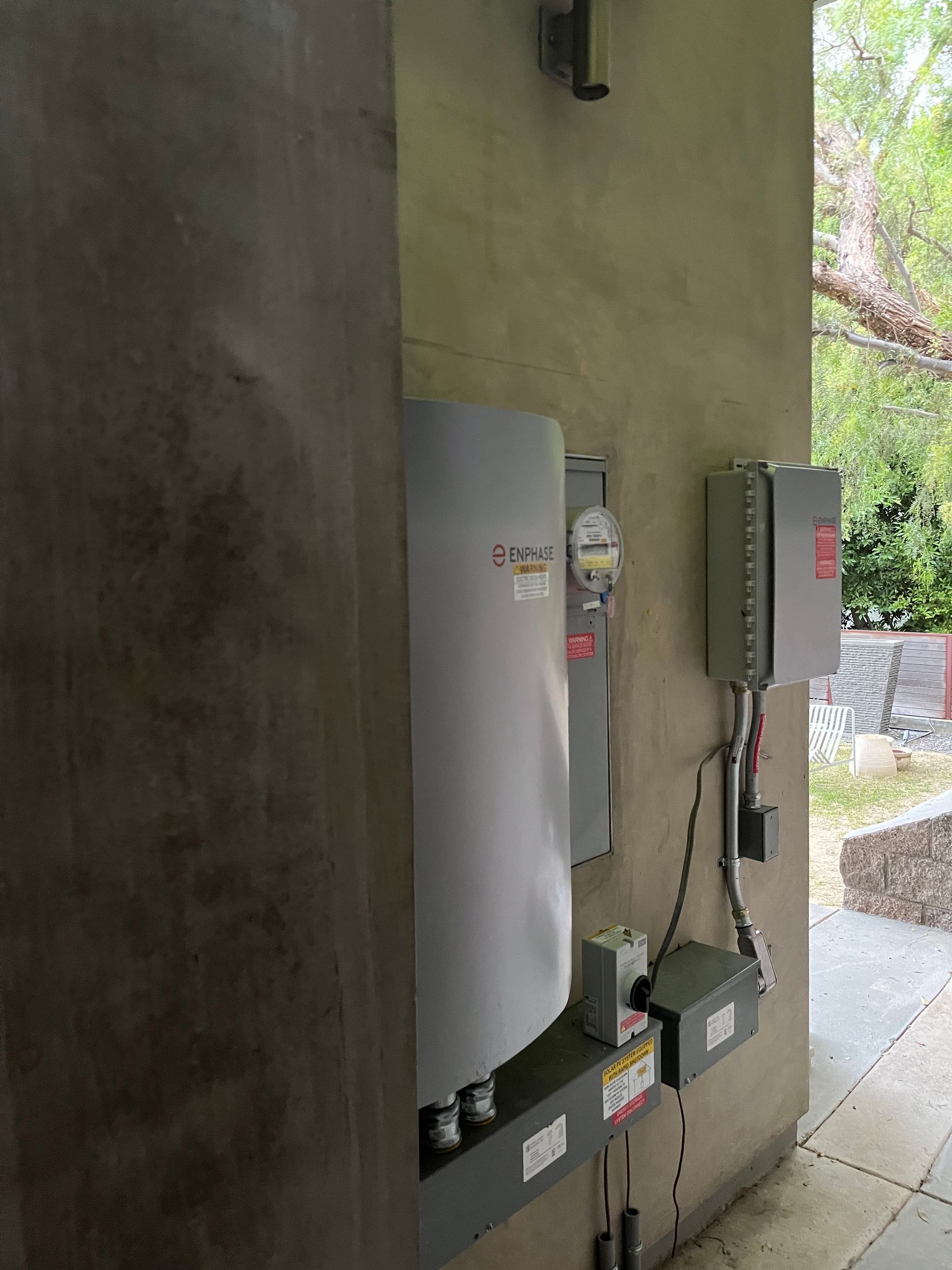 A wall-mounted solar inverter and electrical service equipment, including a utility meter, installed on a concrete wall.