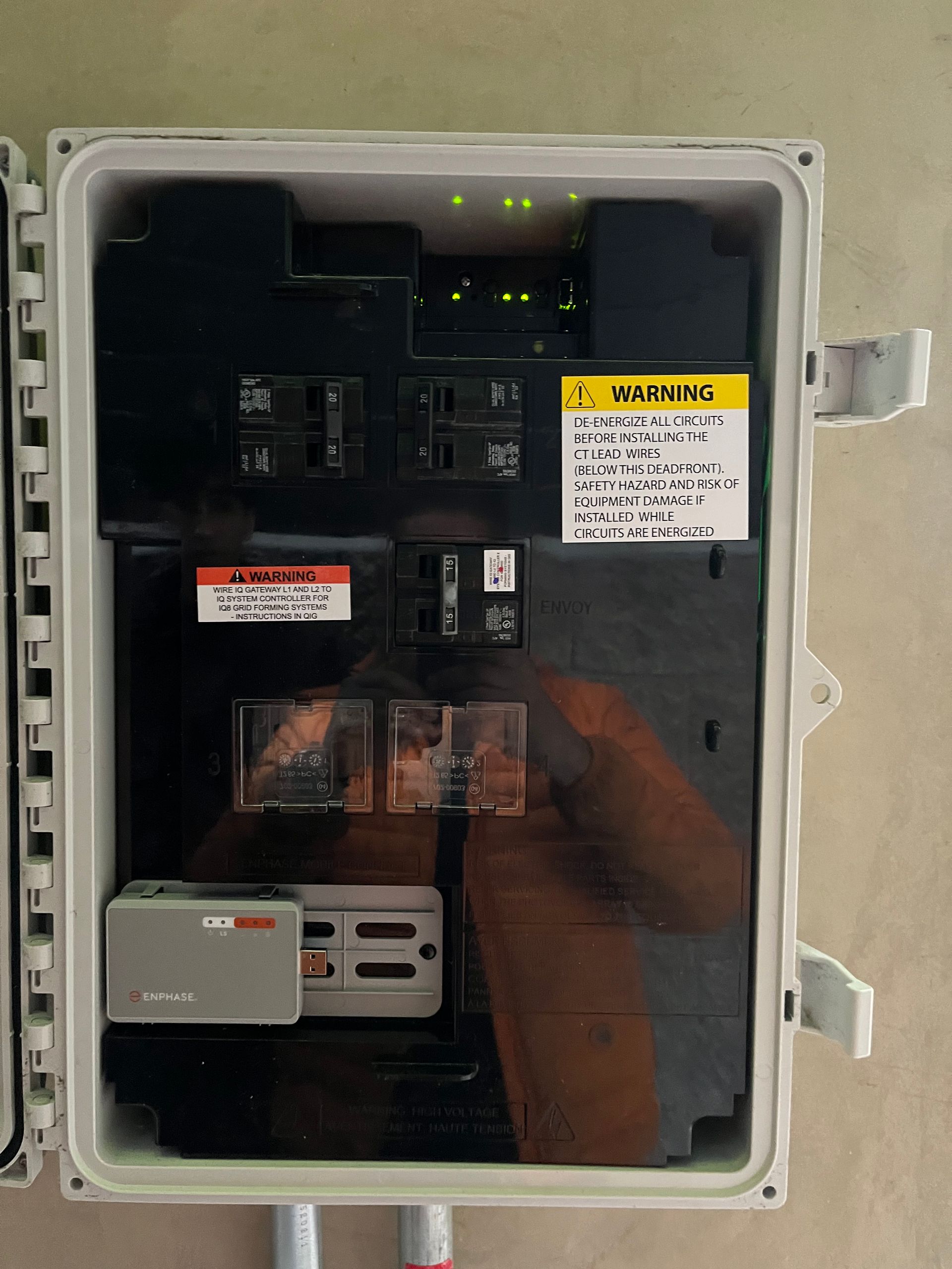 An open wall-mounted electrical panel box with breakers, indicator lights, and a warning label.
