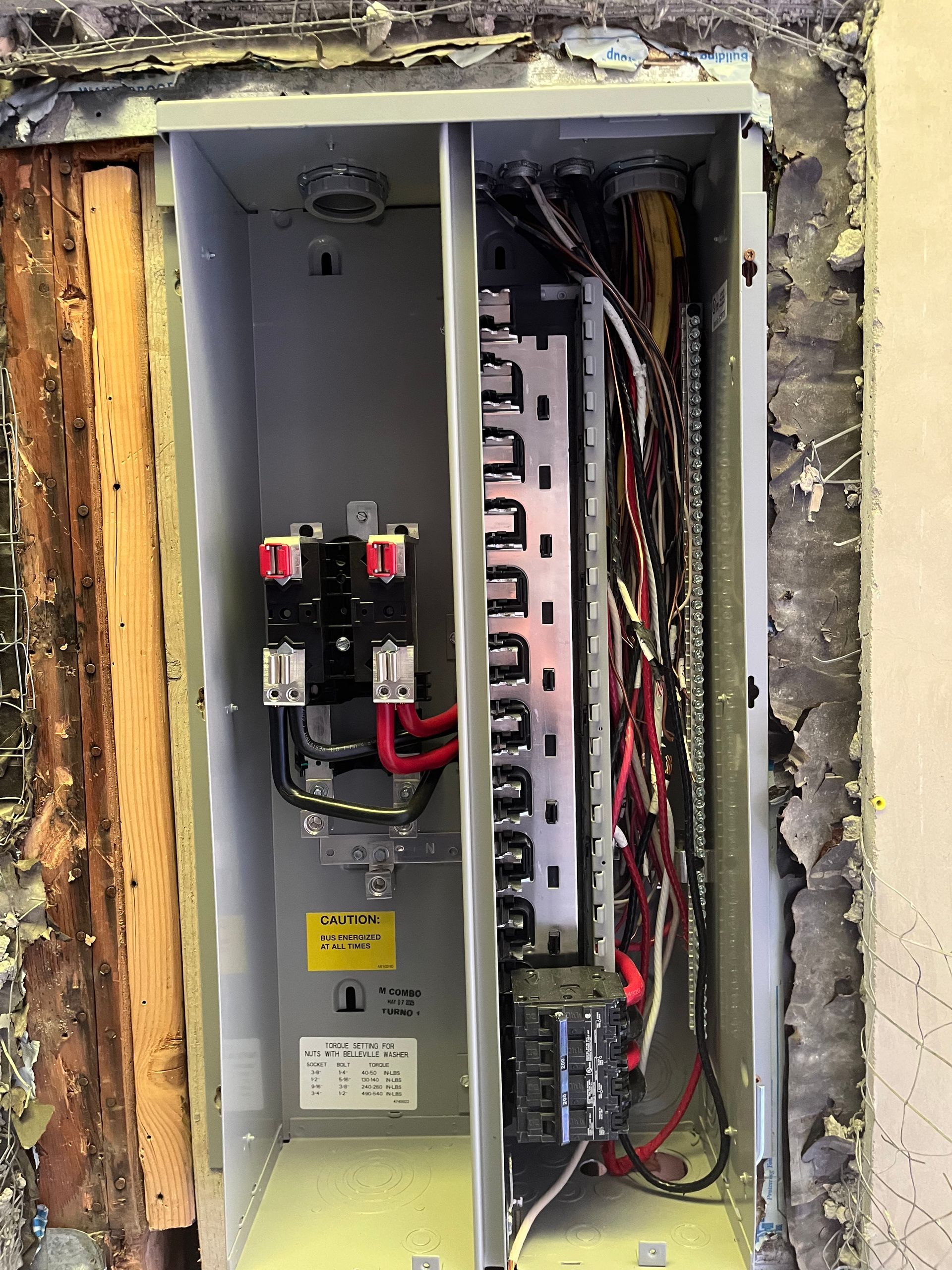 An open electrical panel with visible circuit breakers and wiring inside a wall frame.