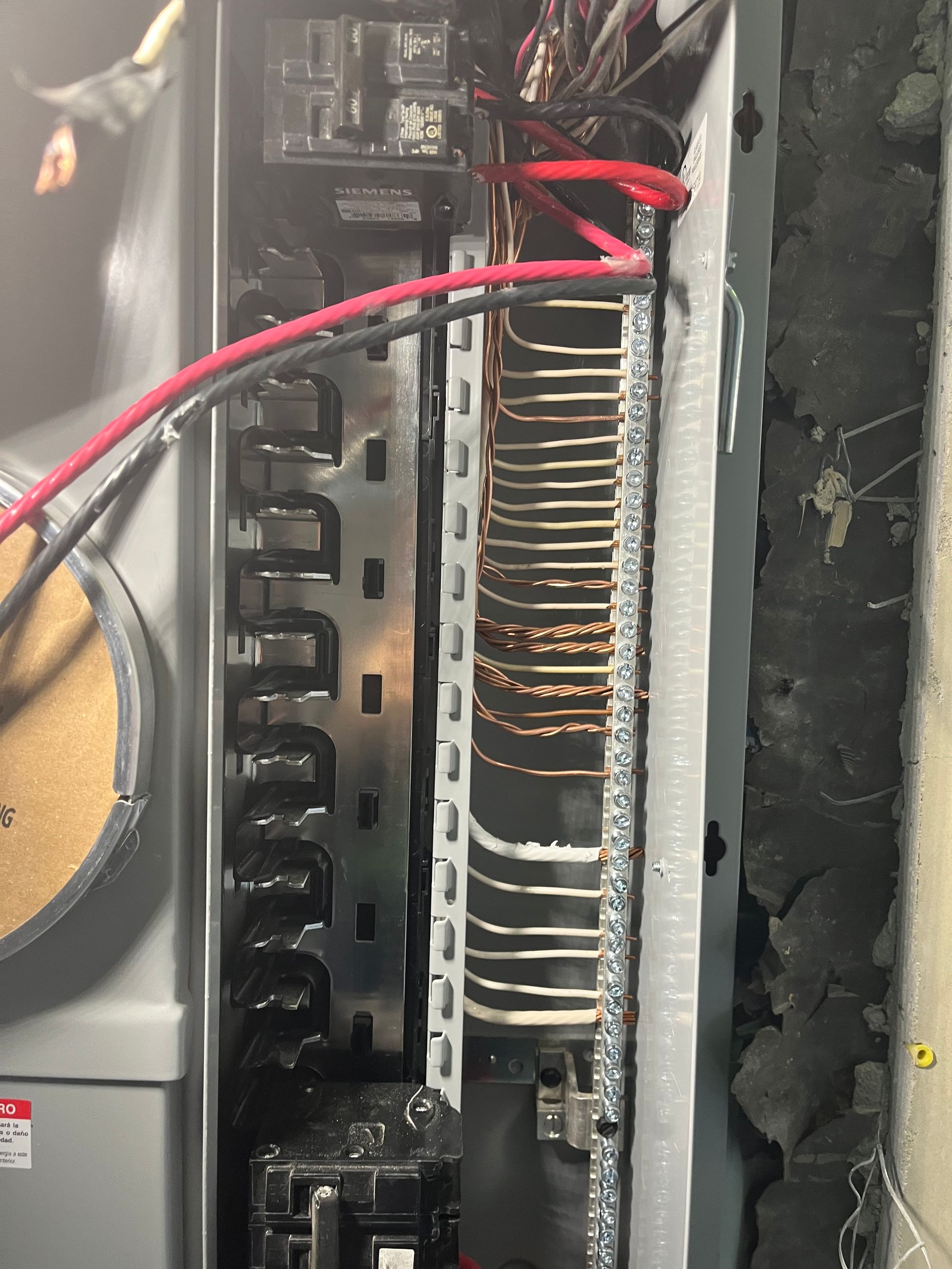 An electrical panel interior showing multiple wires connected to a metal terminal strip and circuit breakers.