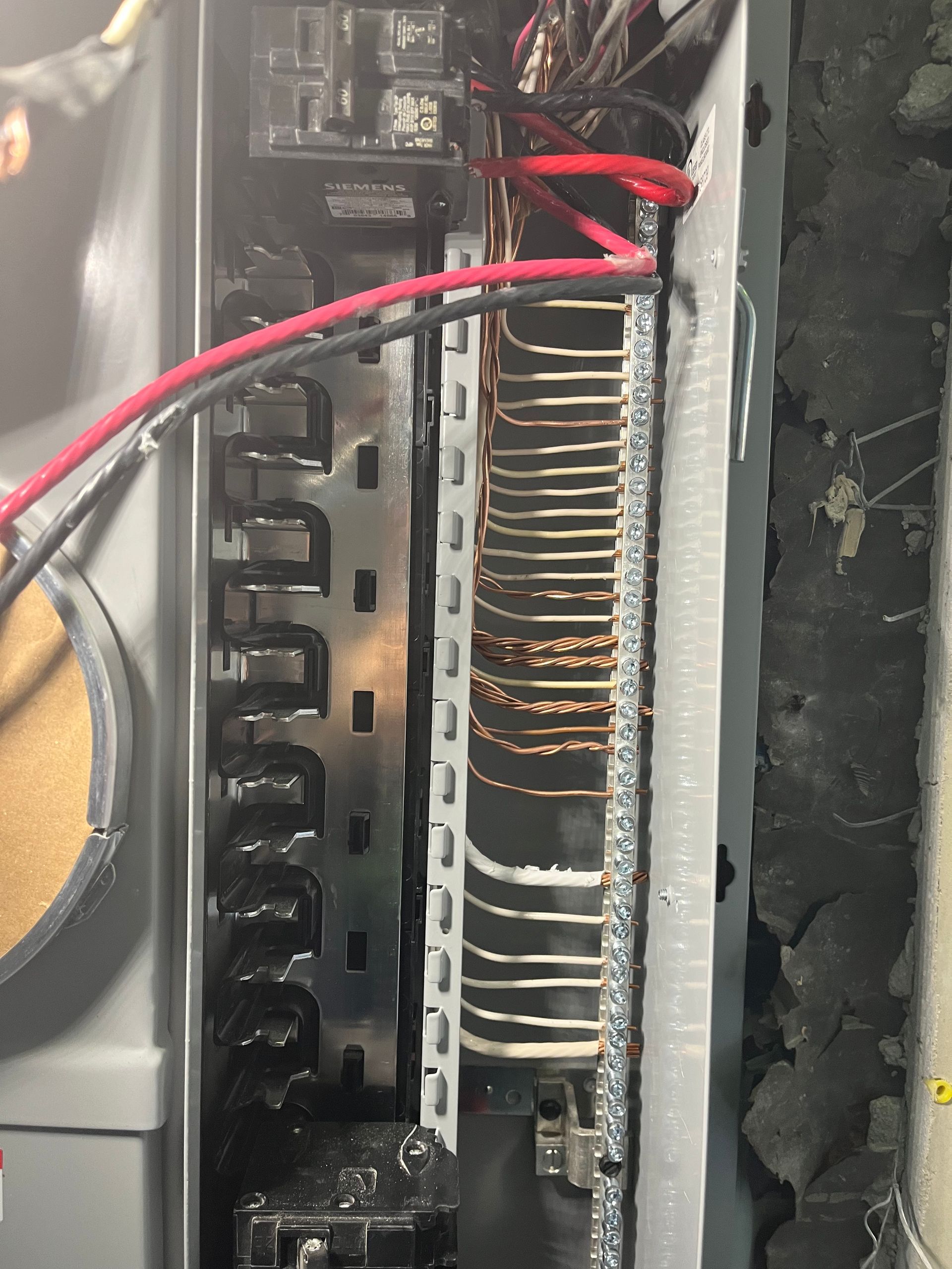 An open electrical breaker box featuring a metal bus bar with numerous copper wires connected to the side terminals.