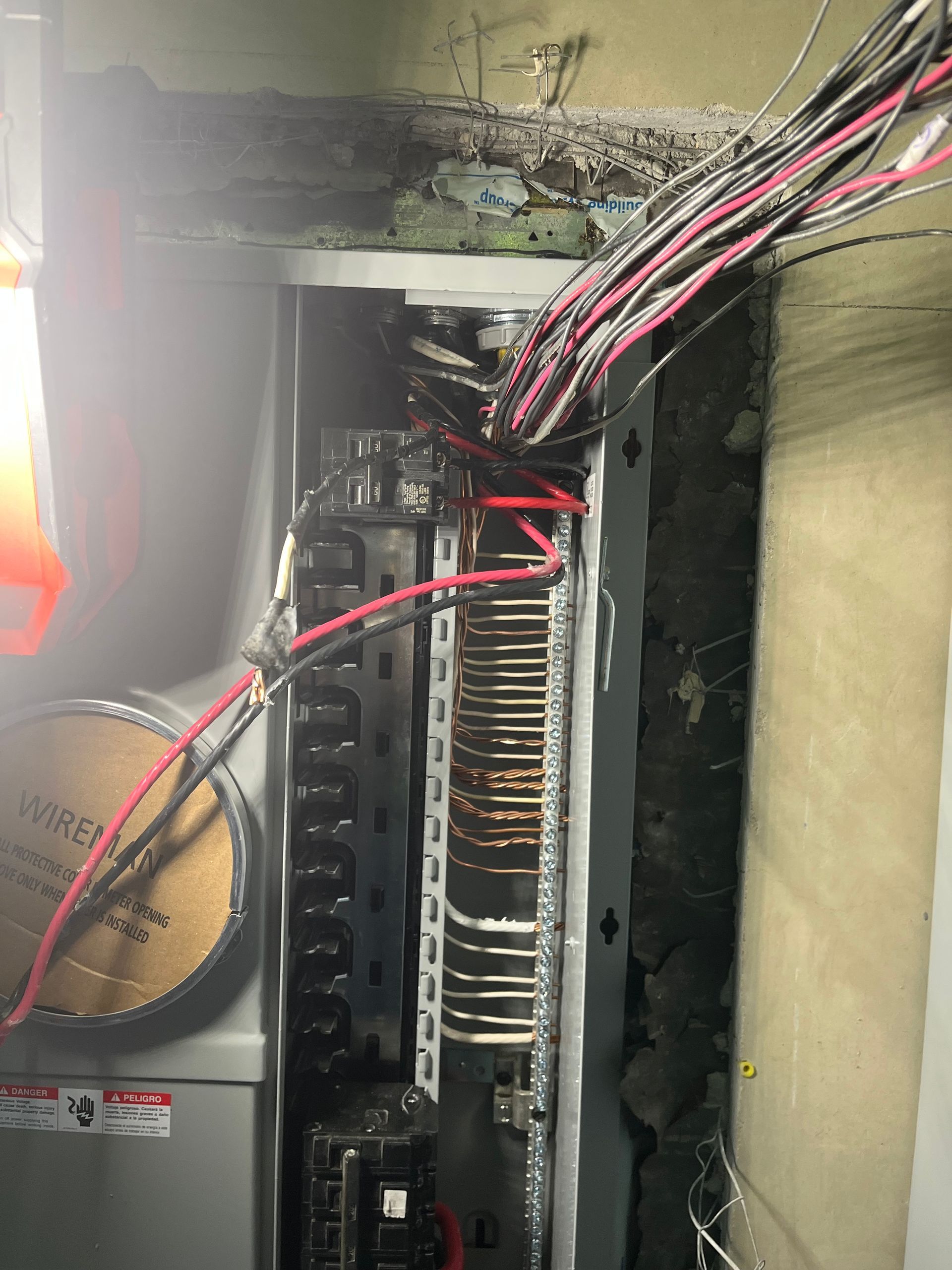 An open electrical breaker panel with numerous colorful wires connected to terminals, mounted on a wall.