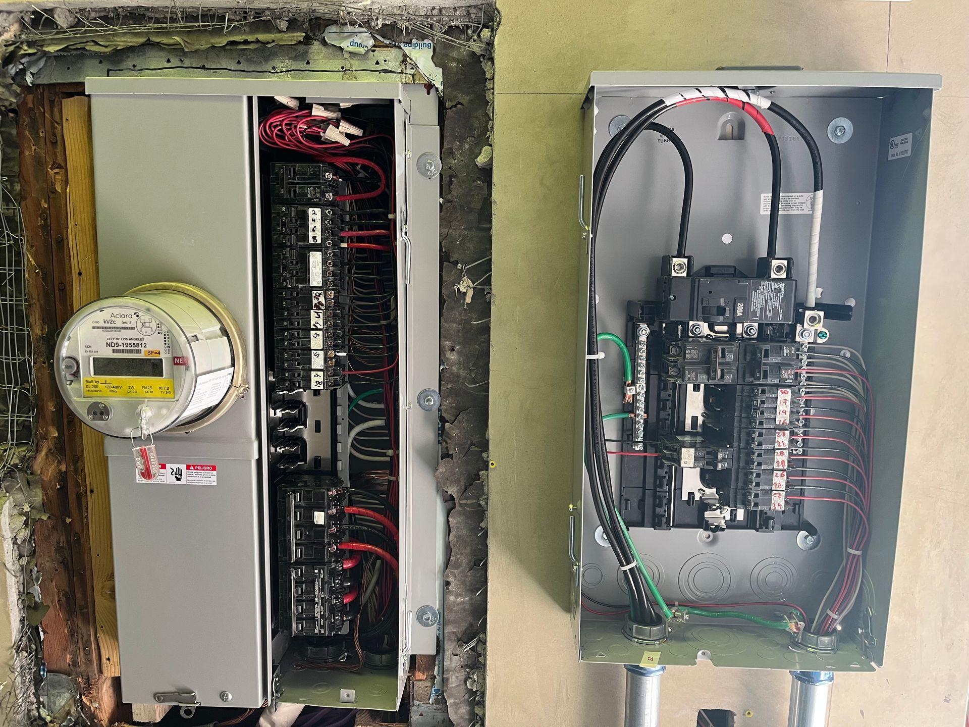 An electrical meter box connected to an open breaker panel on a wall, with visible wiring and components.