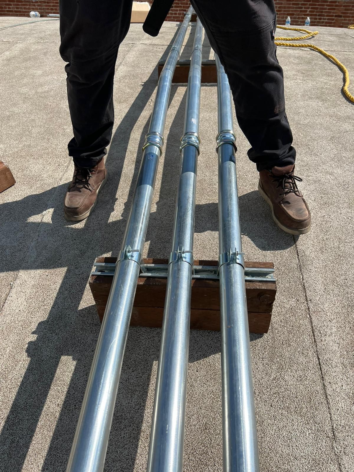 A person stands on a rooftop over three parallel metal conduits mounted on a wooden block base.
