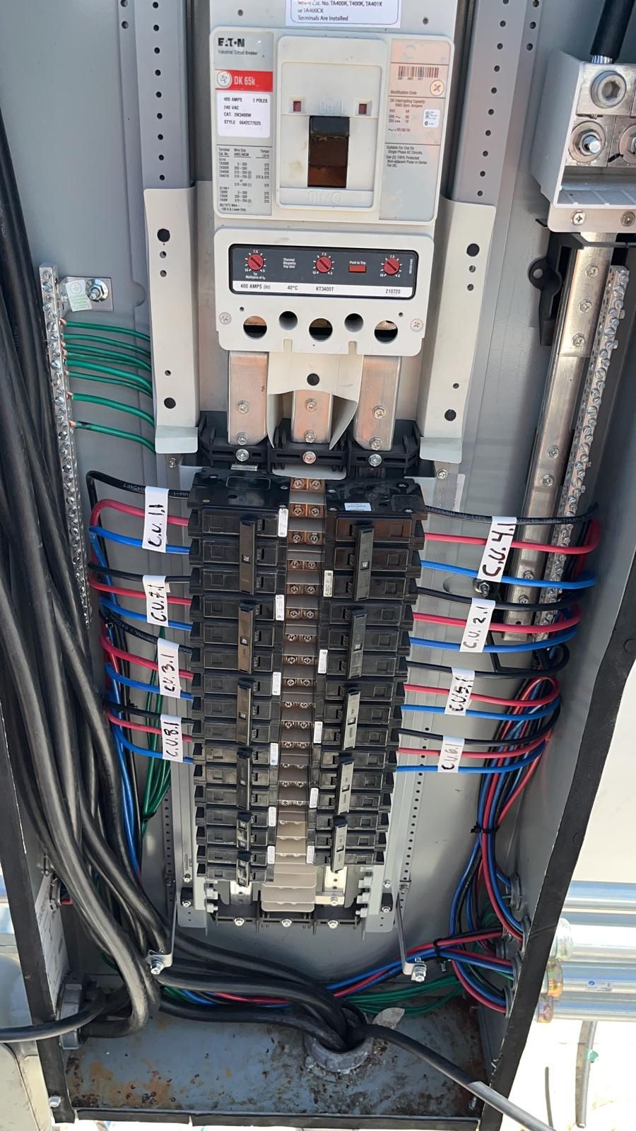 An open electrical panel with a main circuit breaker at the top and multiple wires connected to branch circuit breakers.