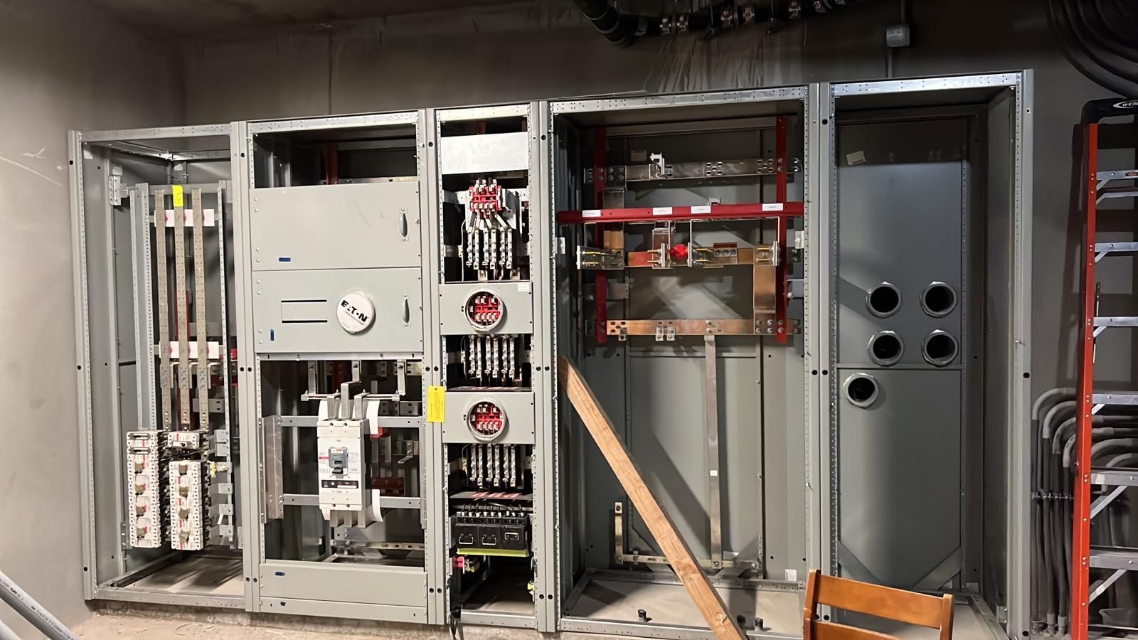 A large industrial electrical switchgear cabinet assembly in an unfinished utility room.