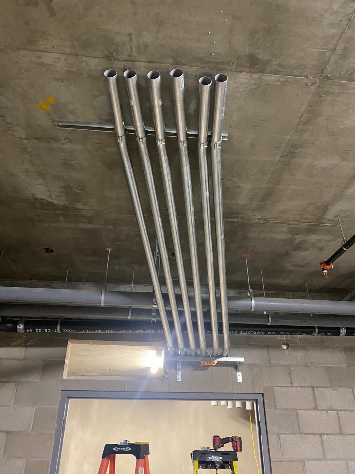 Six metal electrical conduits run parallel along a concrete ceiling above a doorway, supported by a metal bracket.