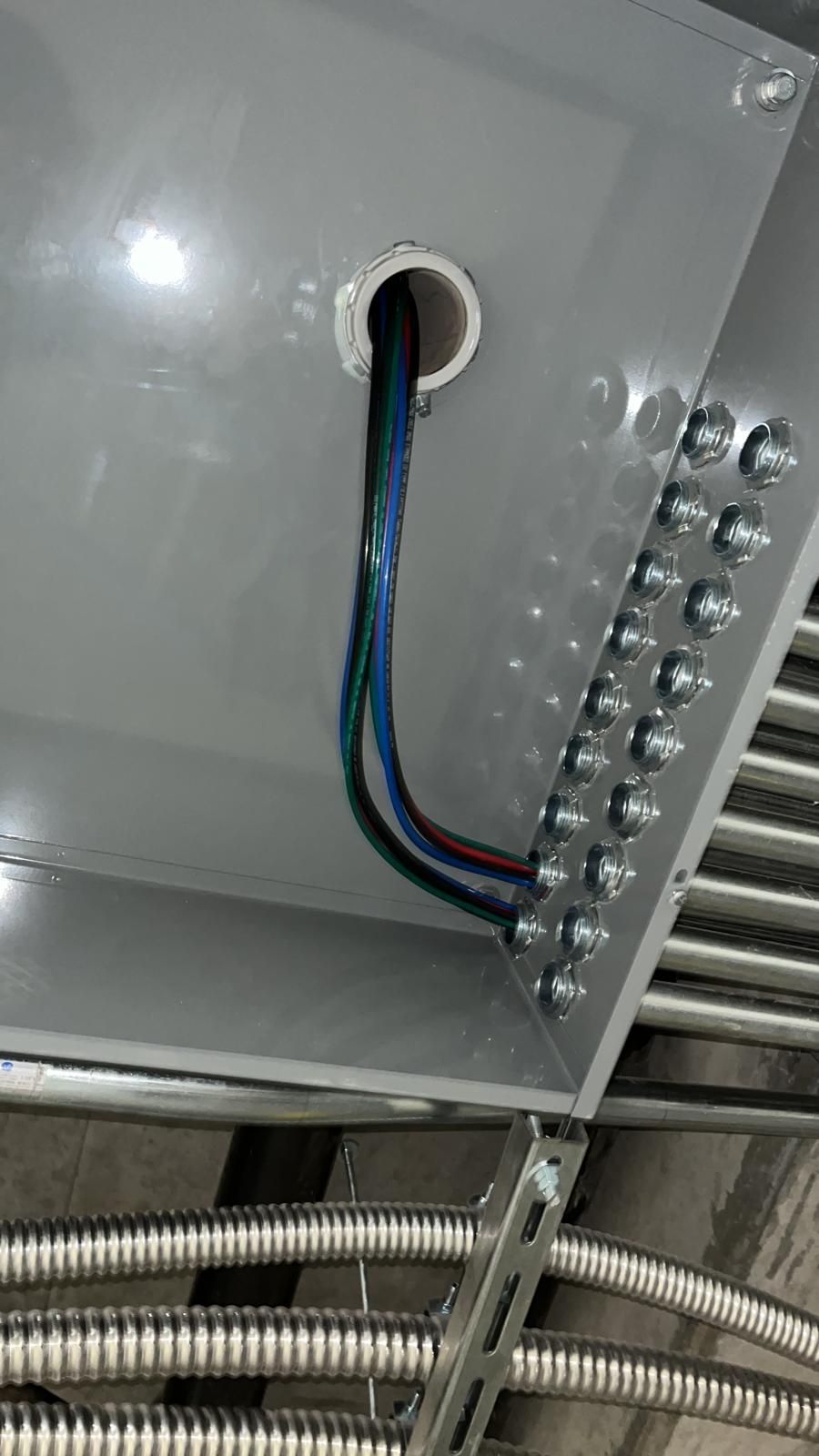 Electrical wires entering a gray junction box from a plastic conduit, with several flexible metal conduits attached nearby.