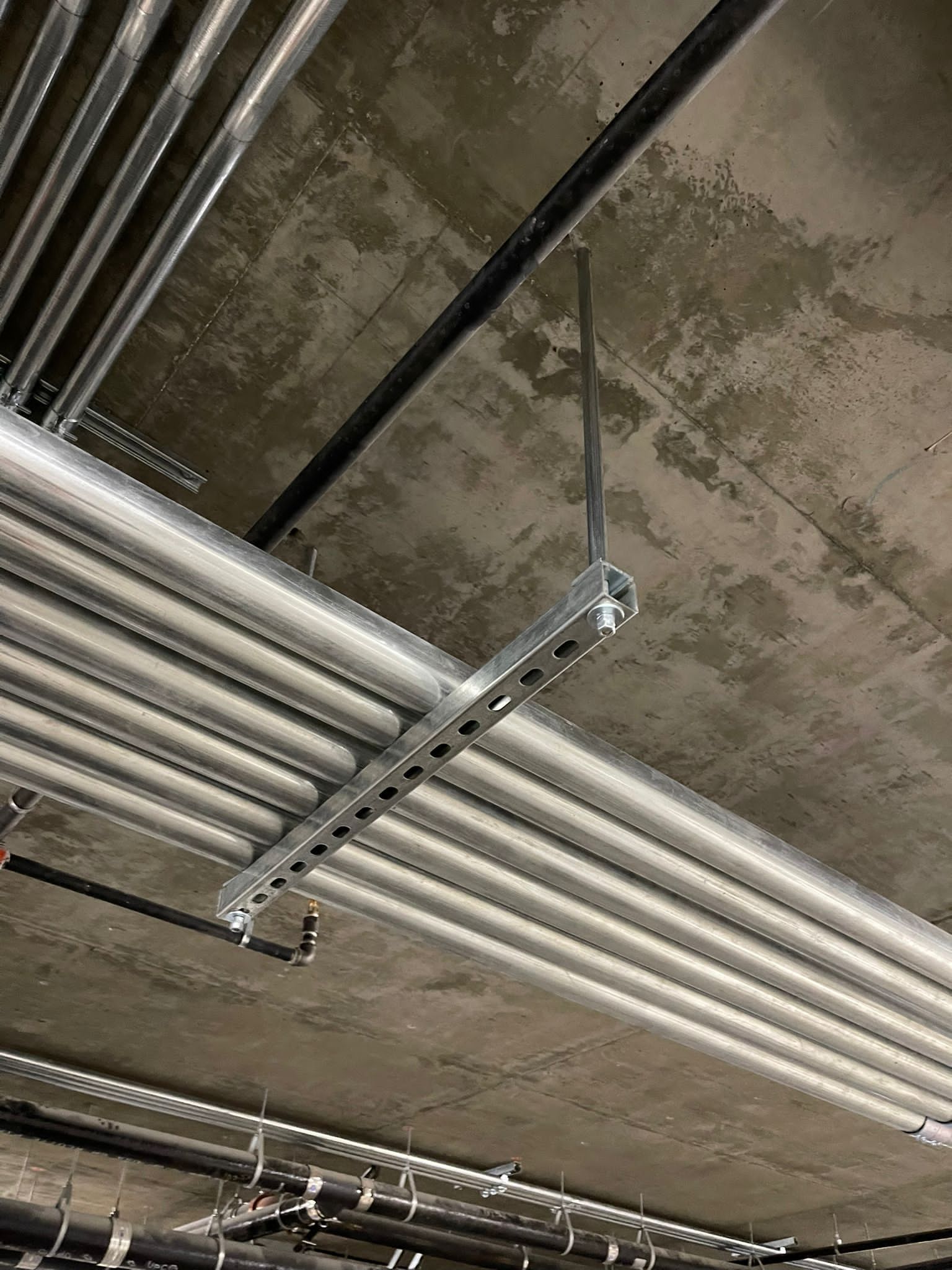 Metal conduits run horizontally along a ceiling, supported by a suspended metal strut channel anchored to concrete.