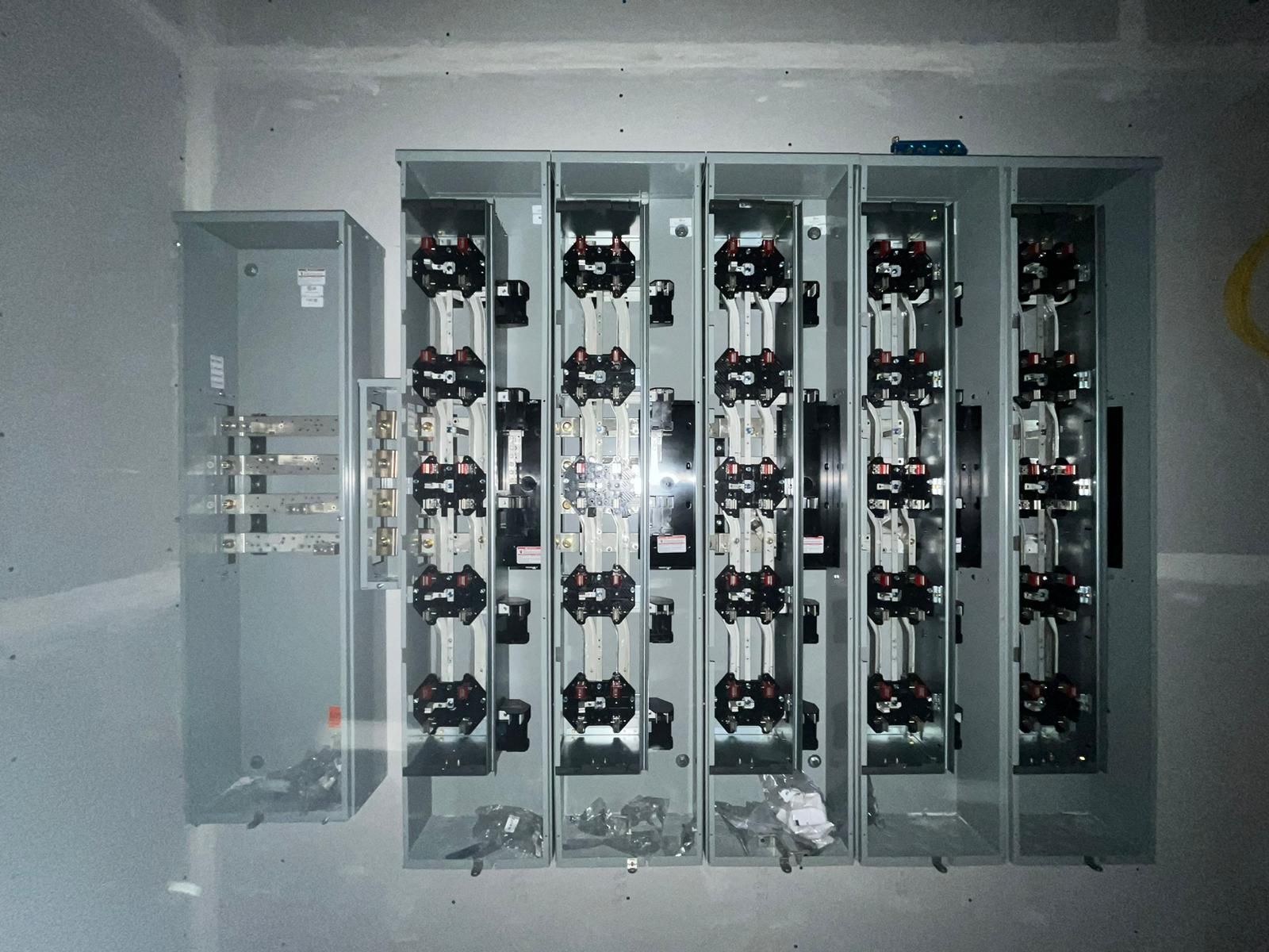 An open electrical meter bank enclosure mounted on a gray wall, featuring multiple empty meter sockets and bus bars.