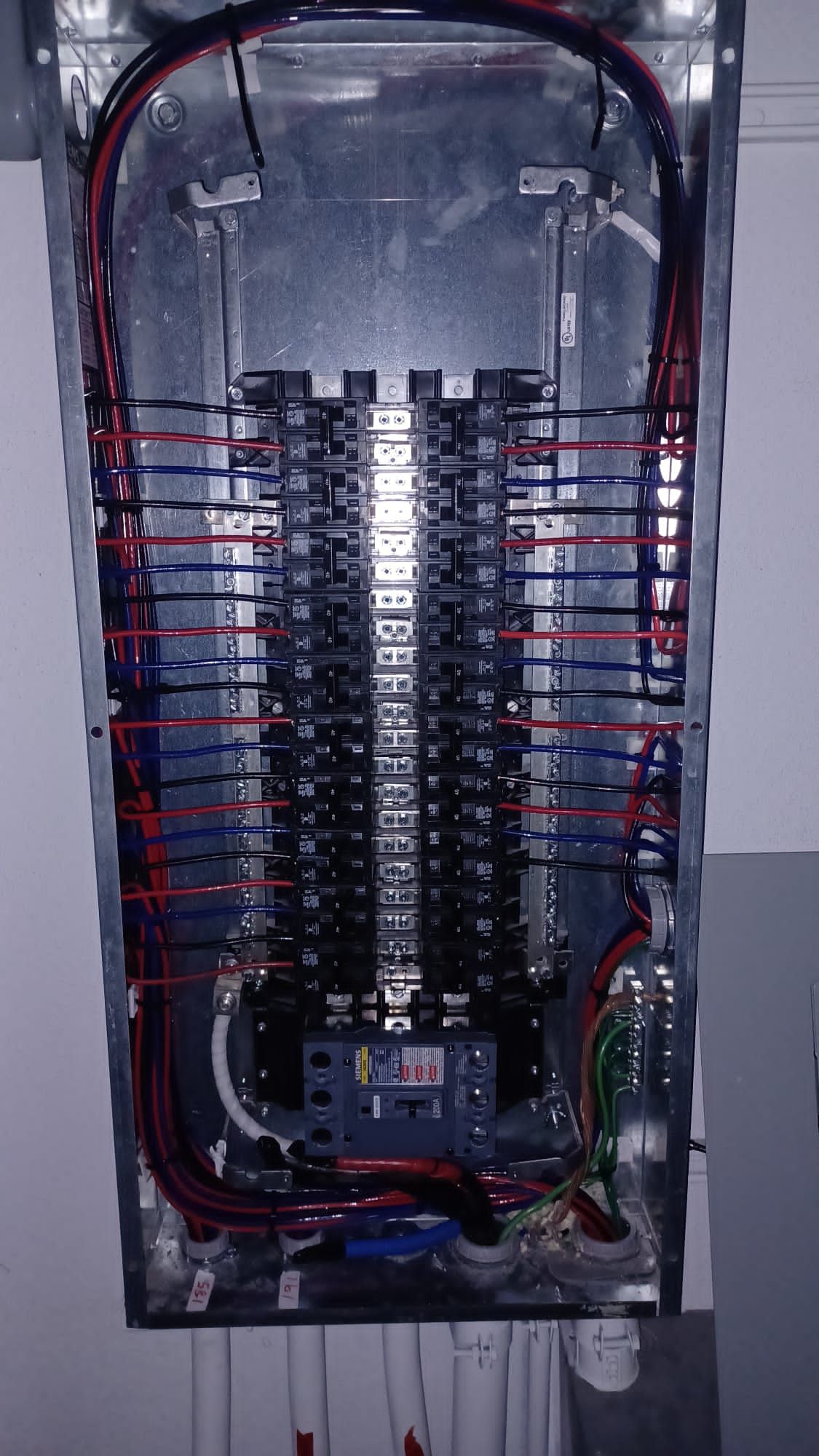 An open electrical panel featuring two columns of circuit breakers with neatly routed black, red, and blue wiring.
