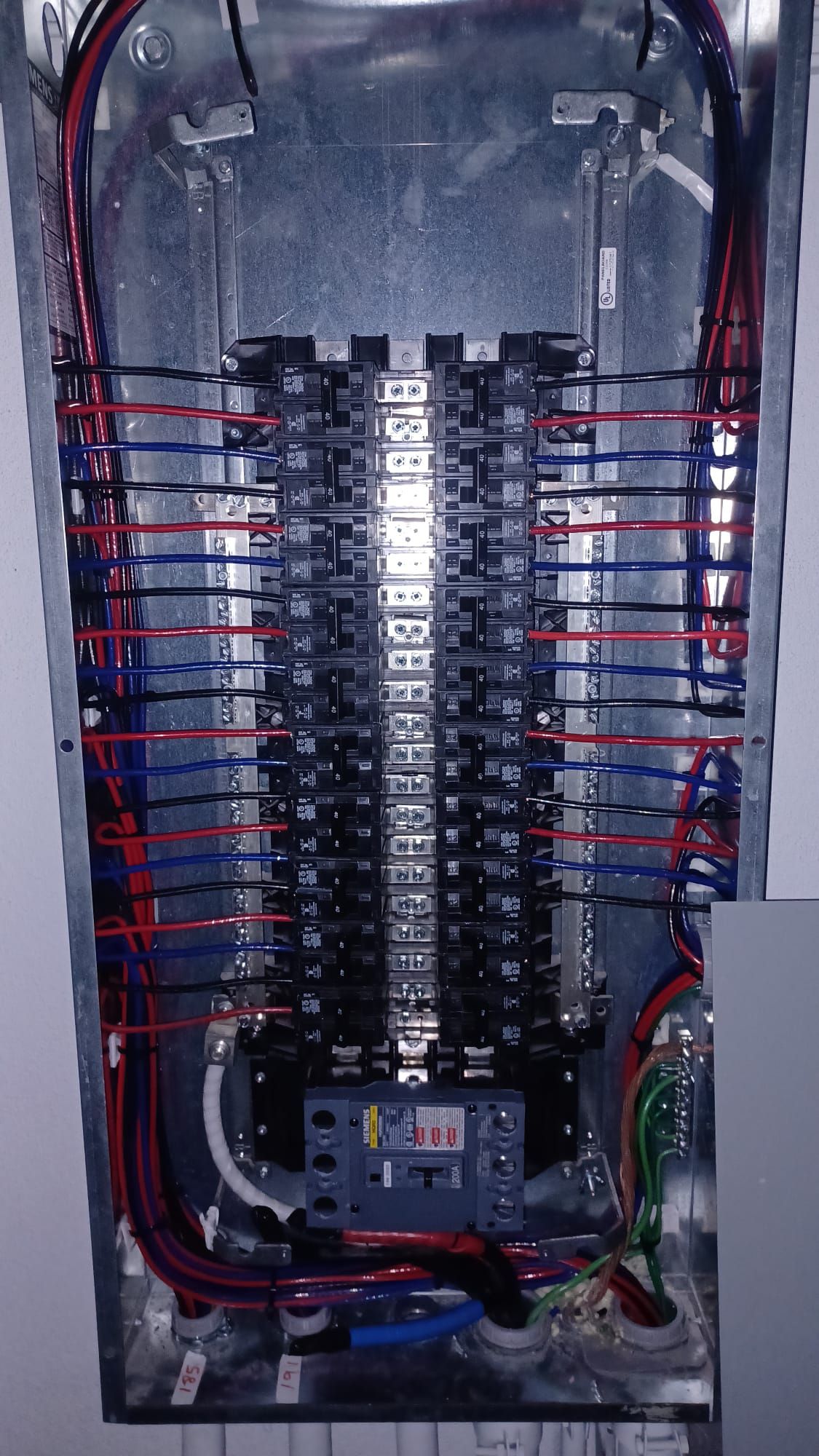 An open metal electrical breaker panel featuring numerous red, black, and blue wires neatly routed to circuit breakers.