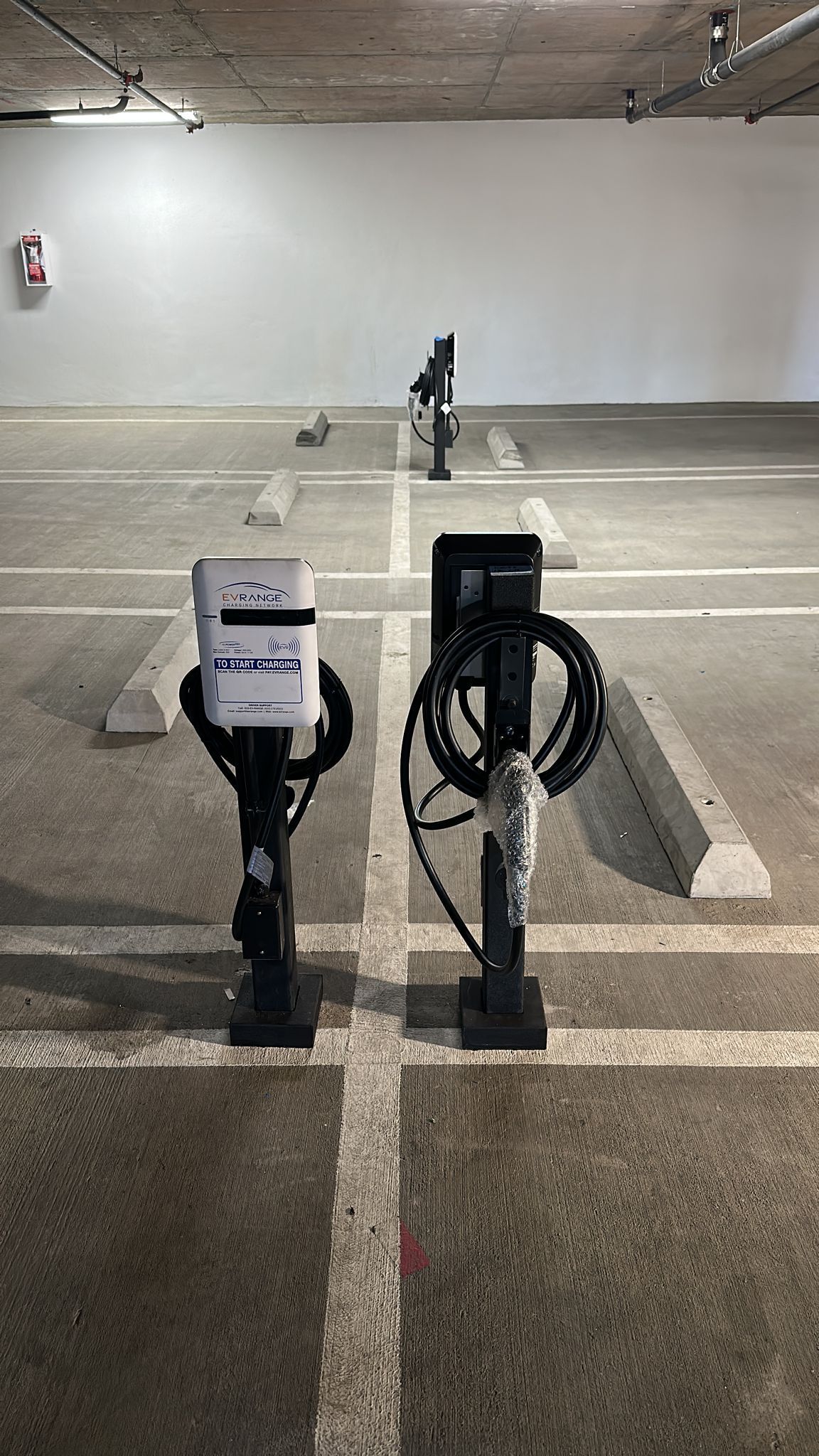Two electric vehicle charging stations stand in an indoor concrete parking garage.