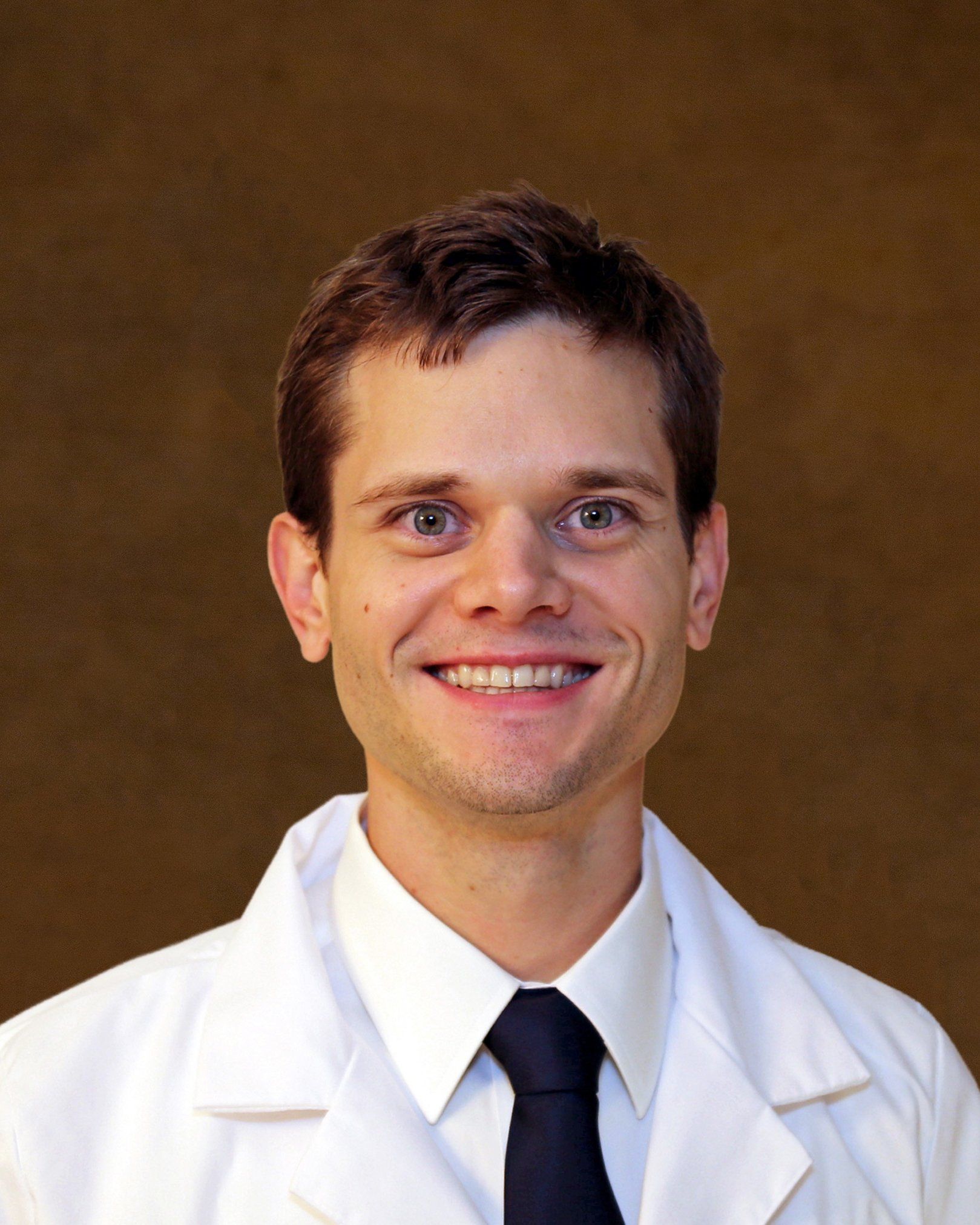 A man in a white coat and tie smiles for the camera