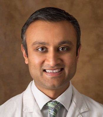 A man in a white coat and tie smiles for the camera