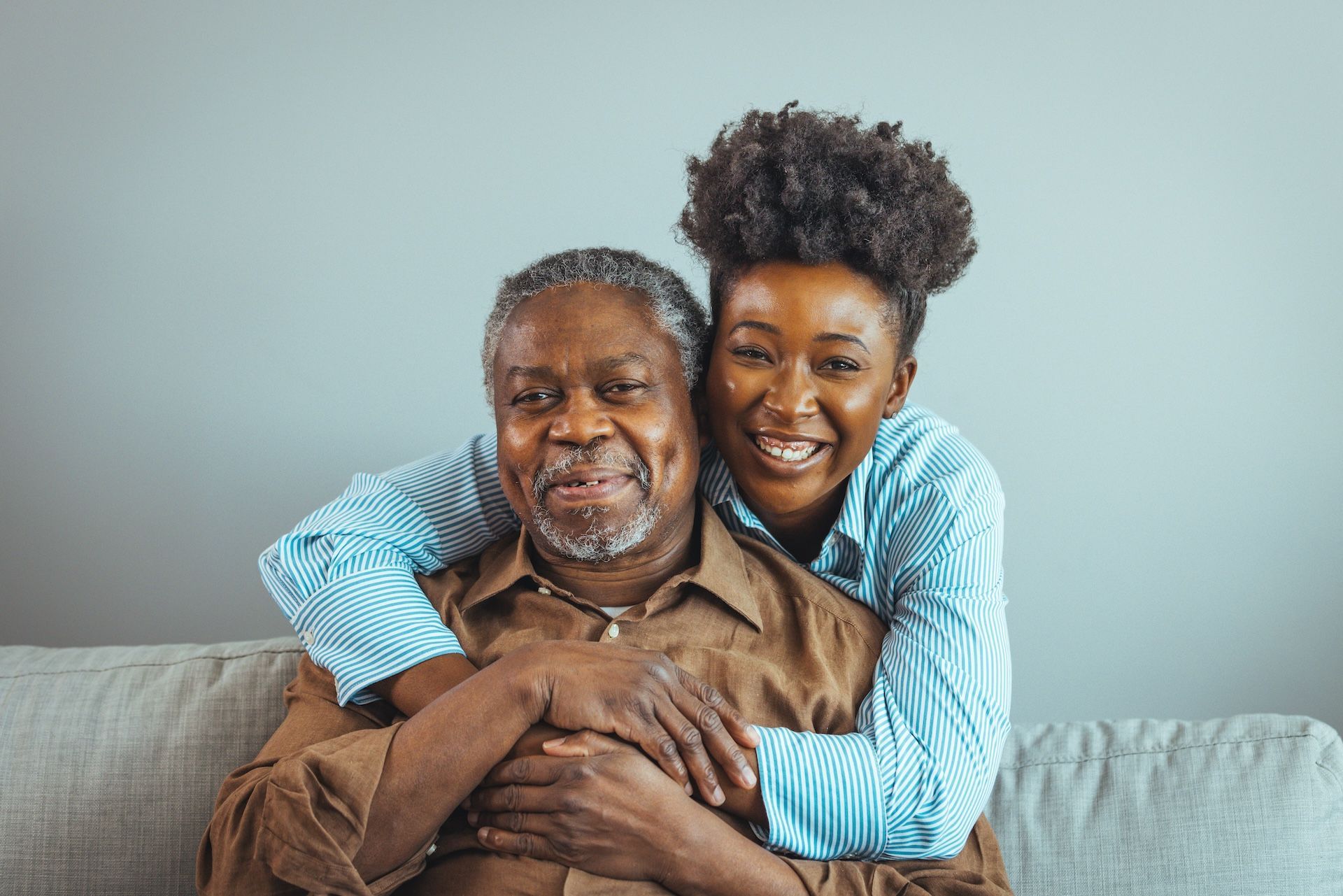 A woman is hugging an older man on a couch.